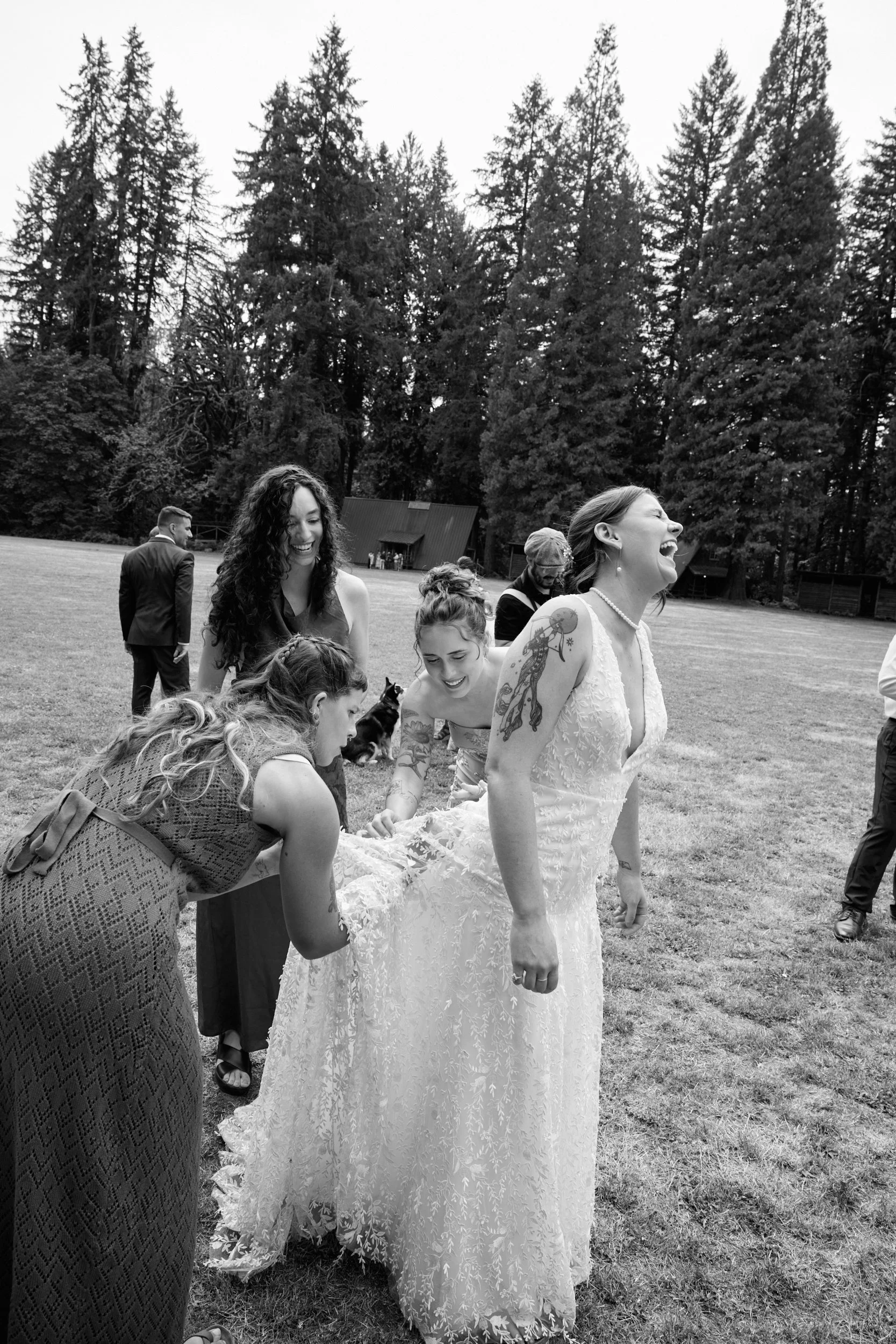 Bridesmaids help a laughing bride remove stinging nettle out of her wedding dress at Camp Namanu near Portland Oregon.