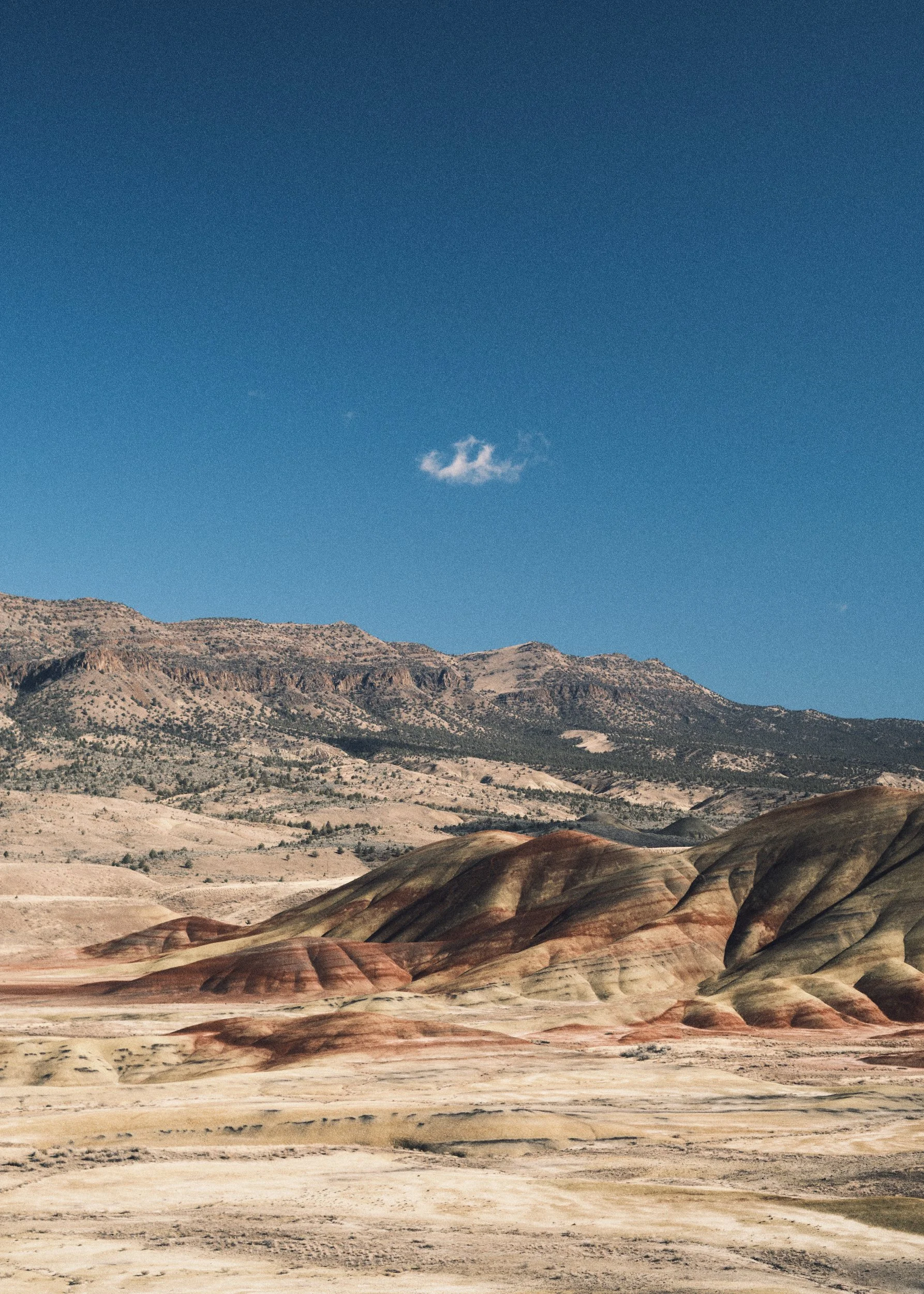 The Painted Hills in Oregon with a lone cloud in the blue sky.