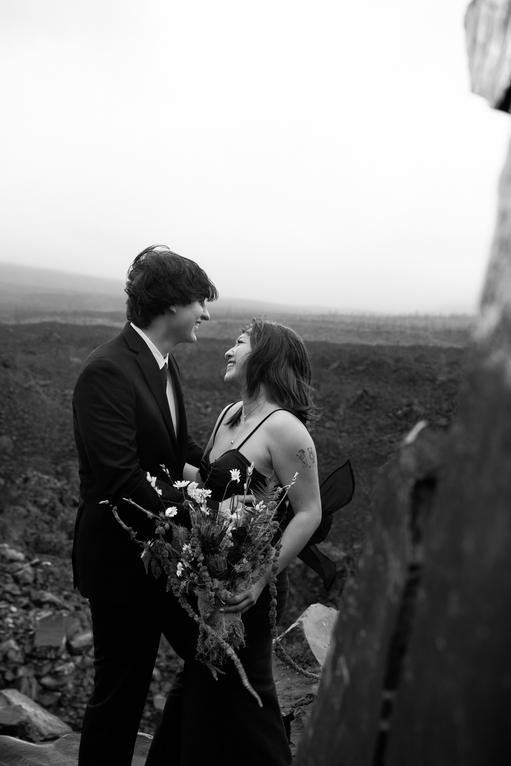 A couple poses for elopement photography at Dee Wright Observatory in Oregon, they both smile while facing each other.