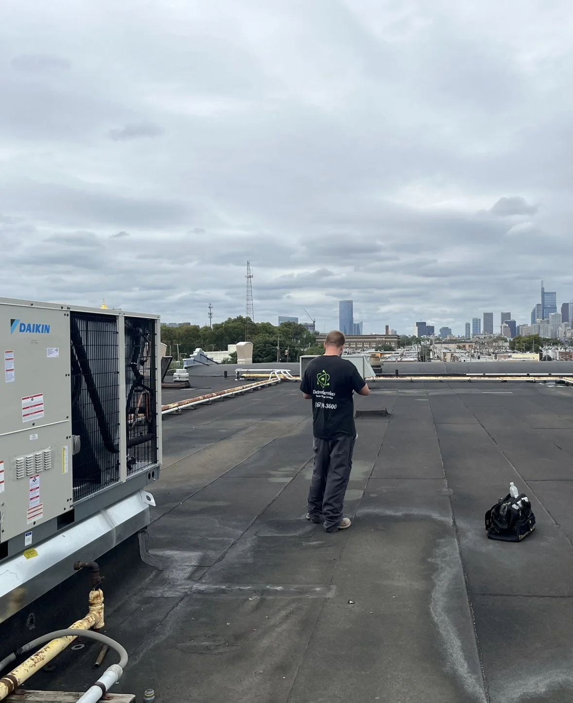 Master Electrician Ed on Fusion Gyms roof doing emergency electrical repair on hvac system with Philadelphia skyline in background