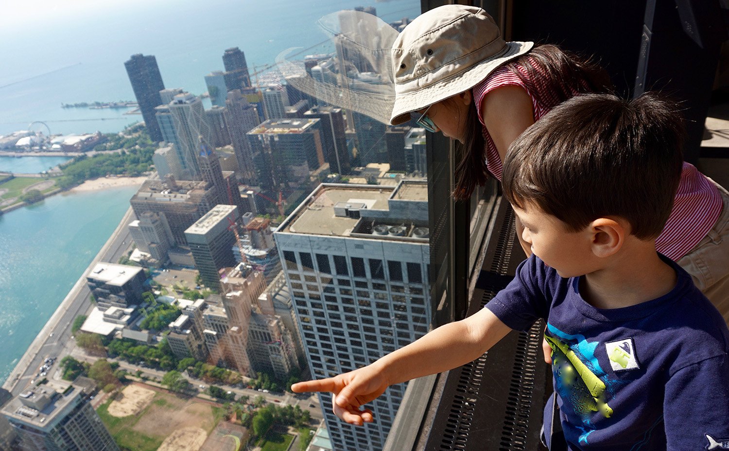 Deux enfants regardant par la fenêtre d'un gratte-ciel vers d'autres bâtiments avec de l'eau en arrière-plan
