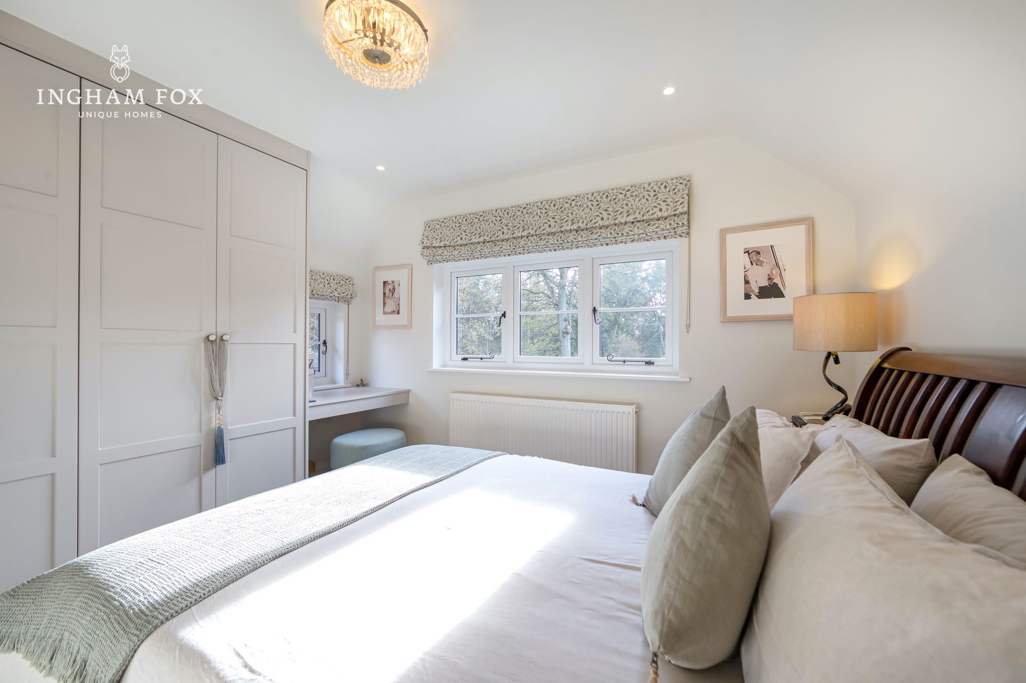 Bright bedroom with double bed, white and pastel decor, large window, plush pillows, bedside lamp, and built-in wardrobe.
