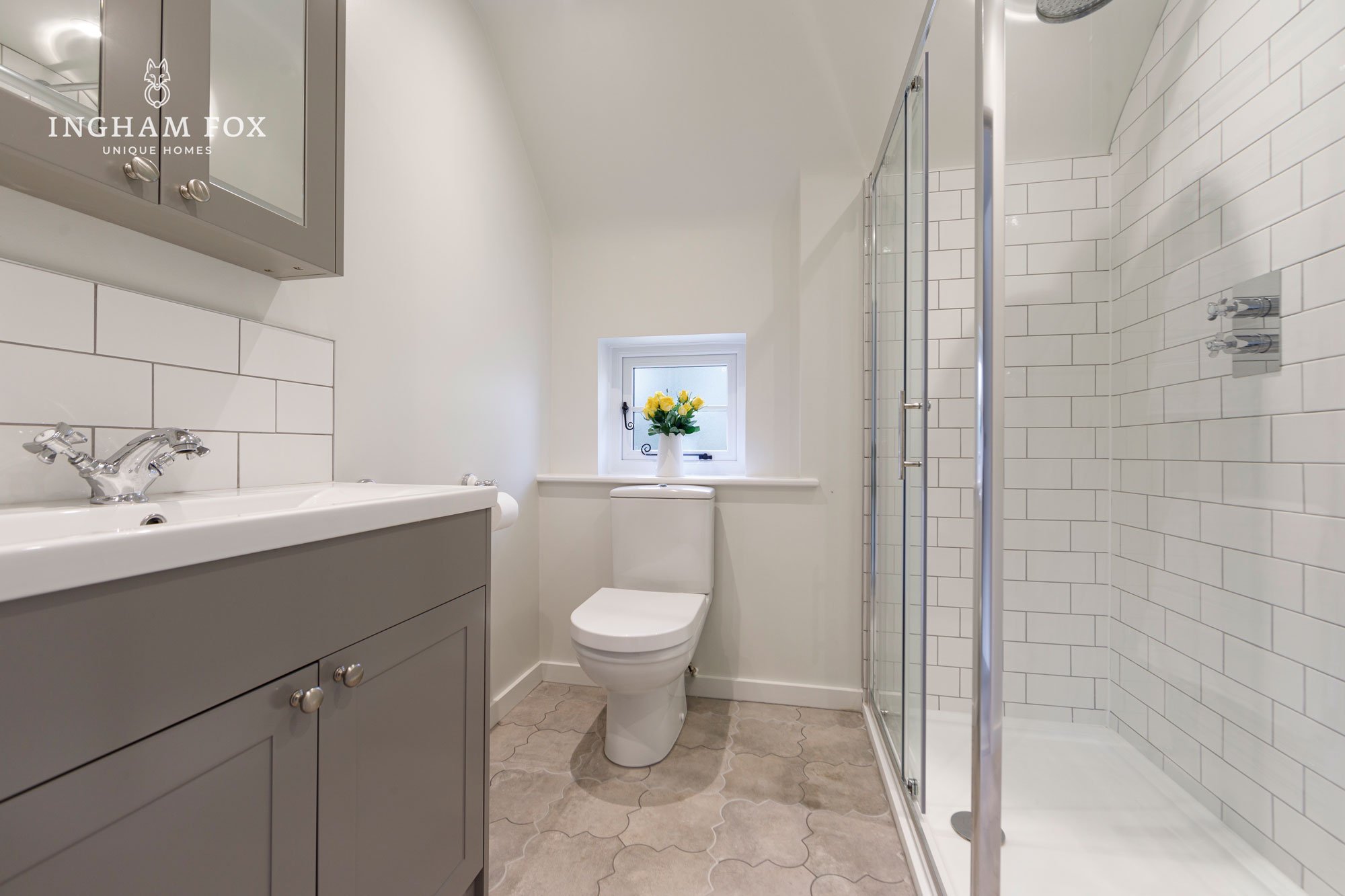 Modern bathroom with gray vanity, white subway tile shower, toilet, small window with yellow flowers.