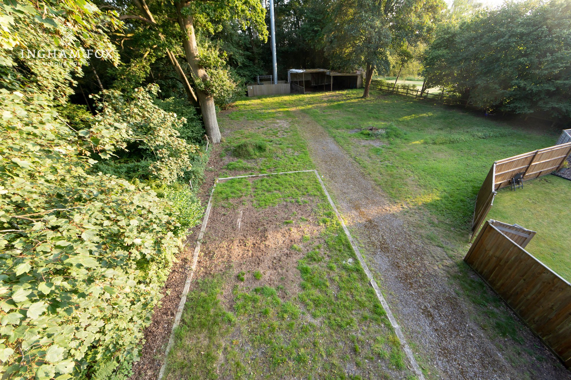 Grassy yard with trees, a gravel path, and a wooden fence.