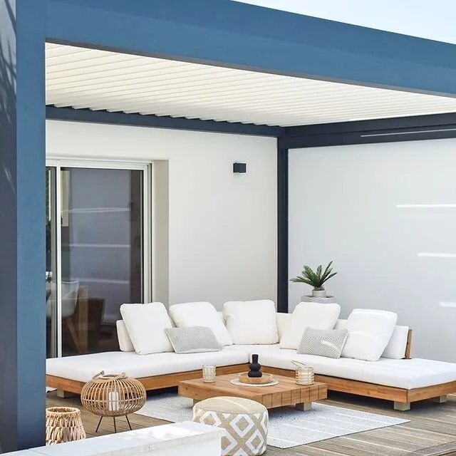 Modern outdoor patio with white sectional sofa, wooden coffee table, and decorative pillows, under a pergola.