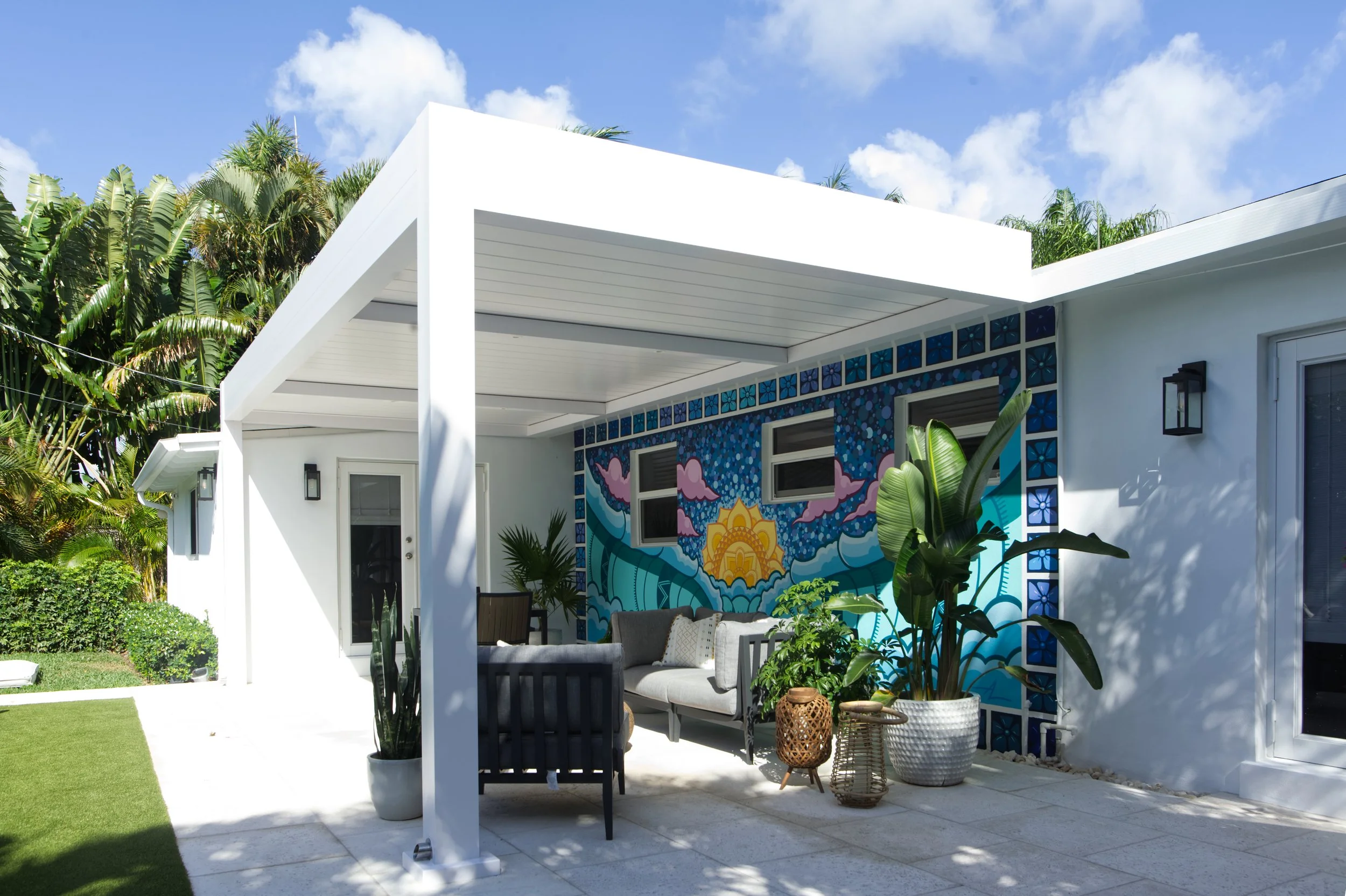 Outdoor patio with white pergola, colorful mural, and plants.