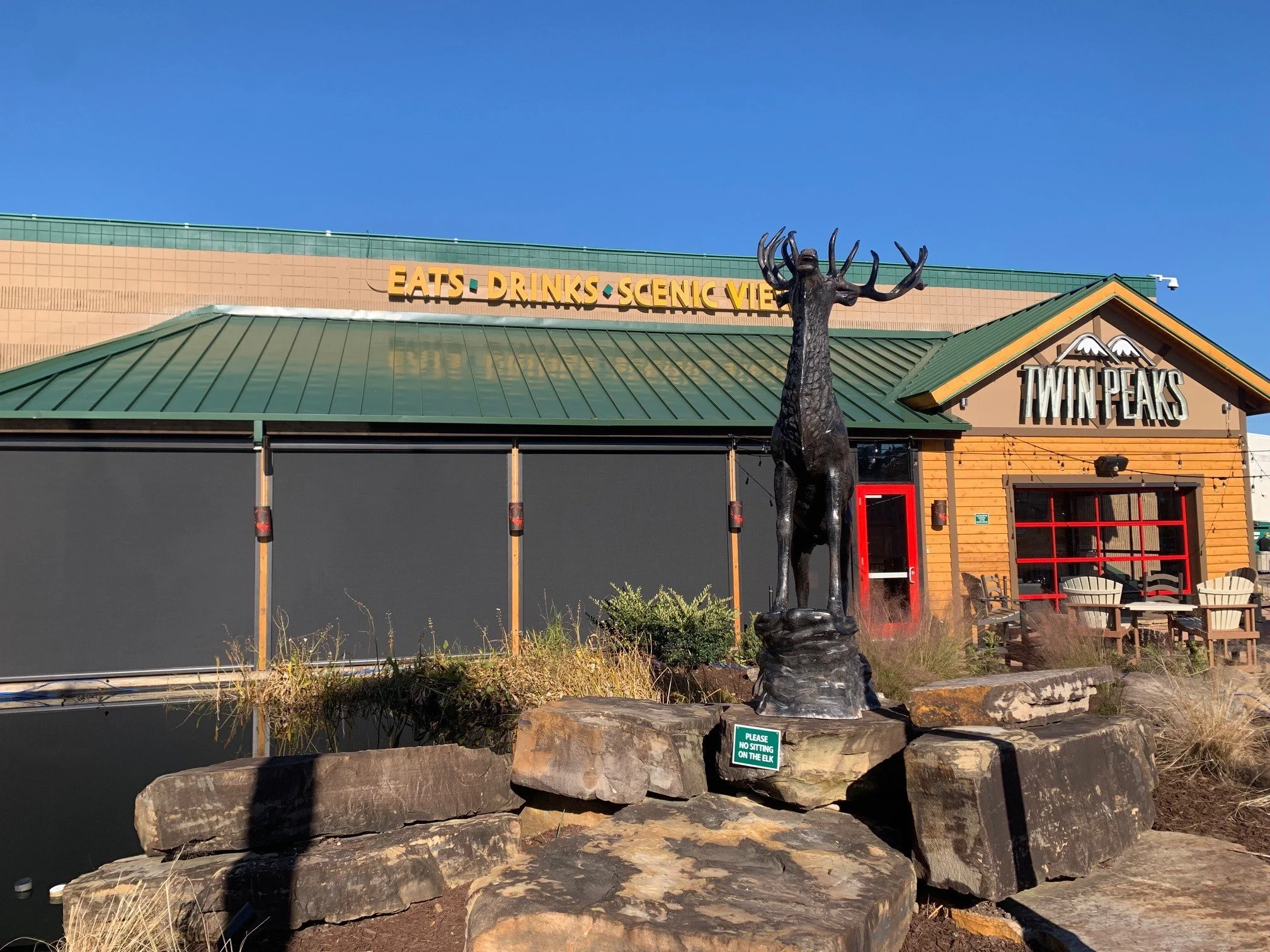 Exterior of Twin Peaks restaurant with moose statue and green roof.