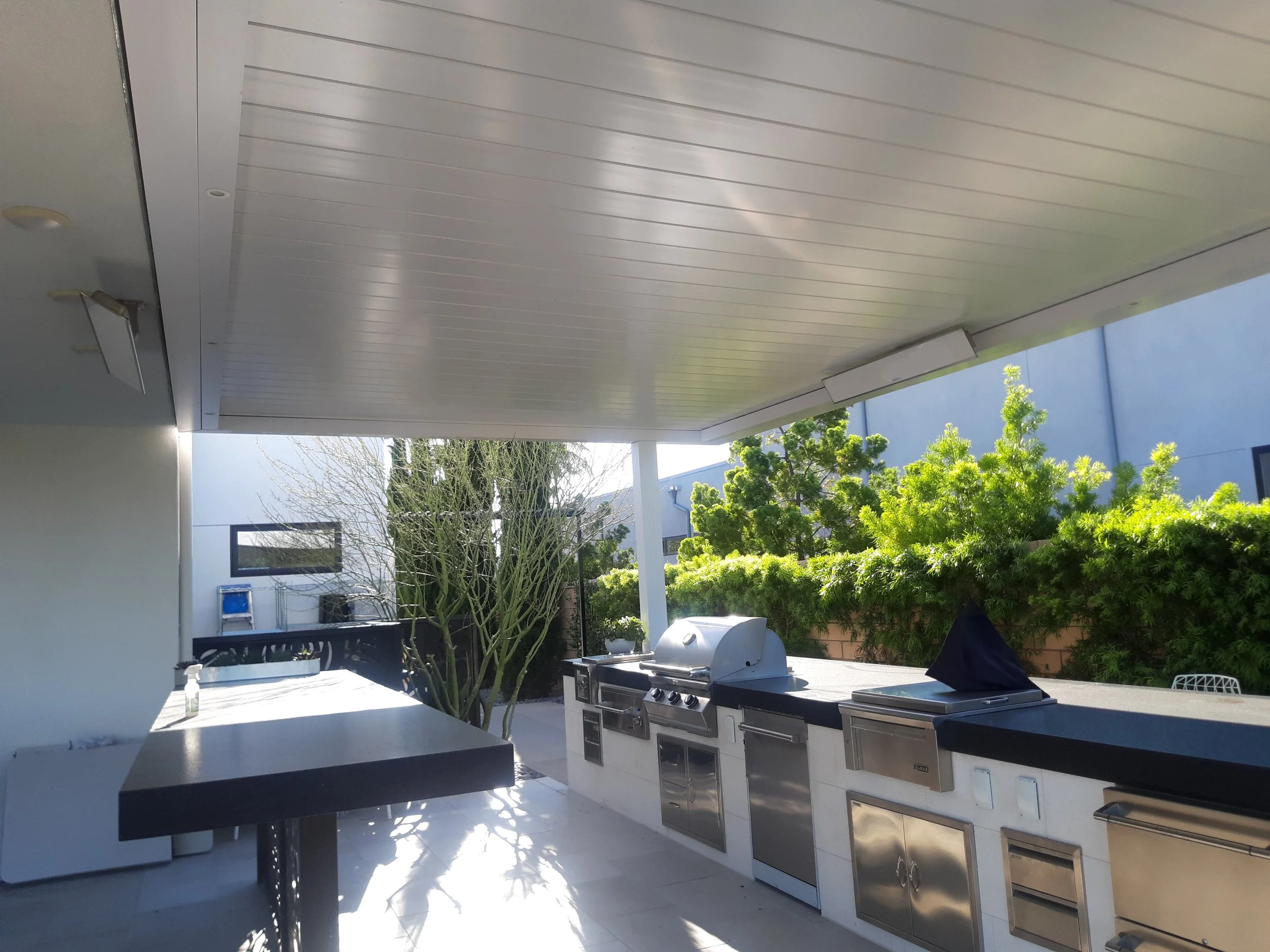Outdoor kitchen with stainless steel appliances, covered patio, and surrounding greenery.