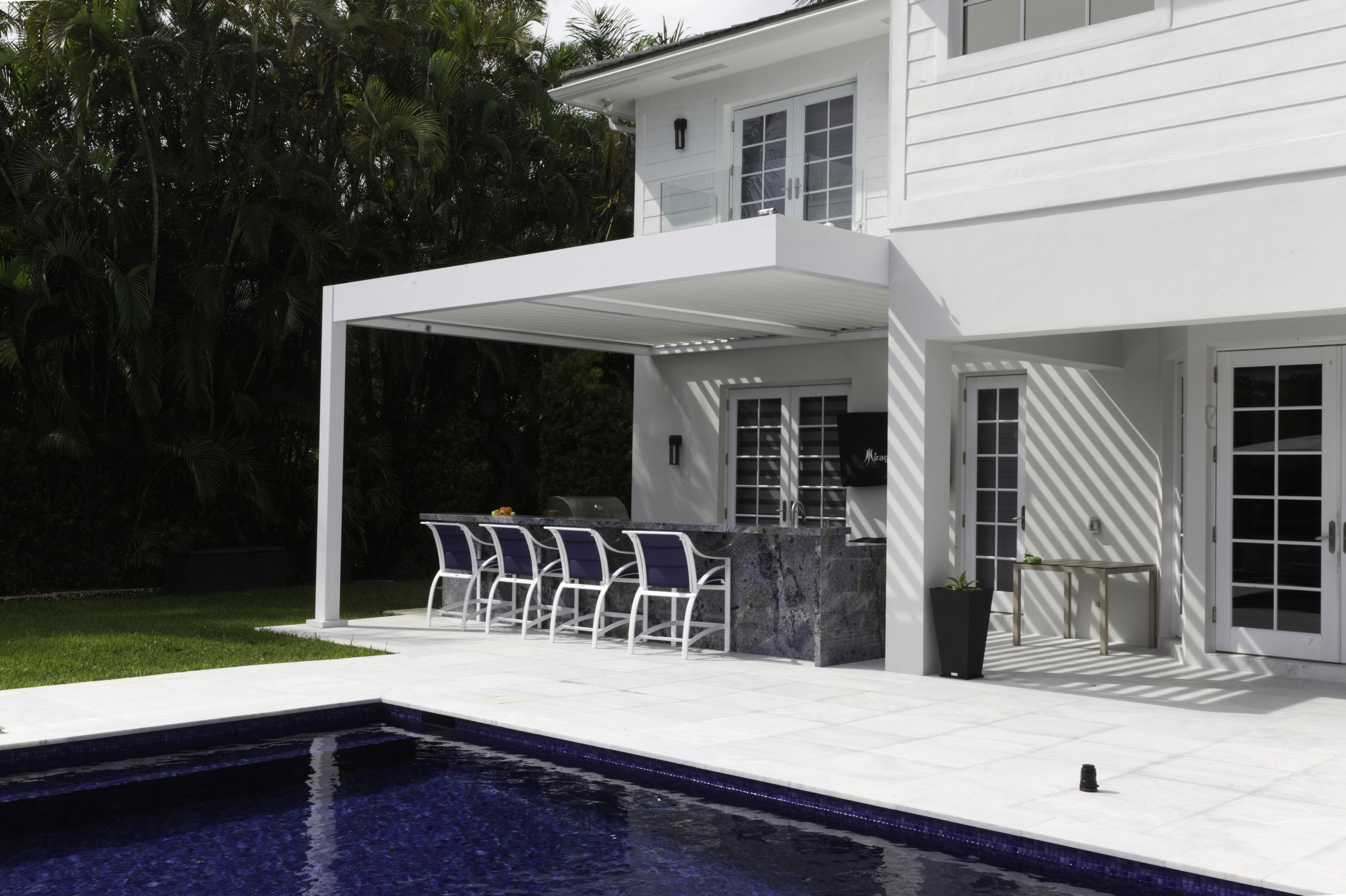 Modern backyard with swimming pool, patio with chairs, and a white two-story house.