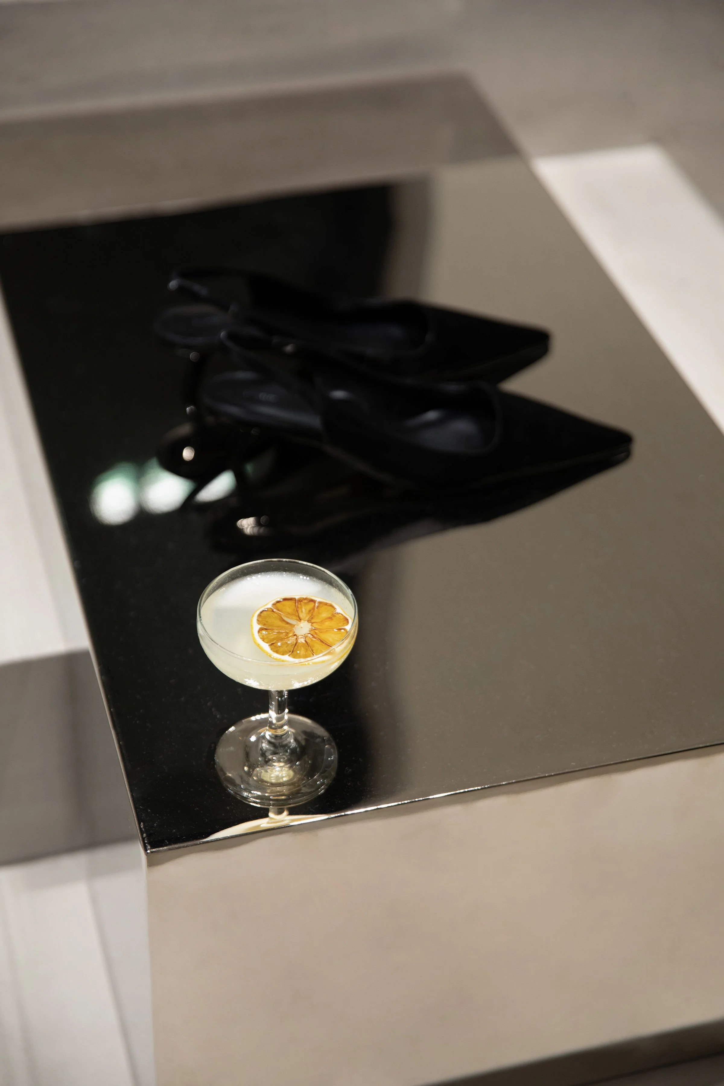 A cocktail glass with a lemon slice garnish on a black countertop, with black sunglasses in the background.