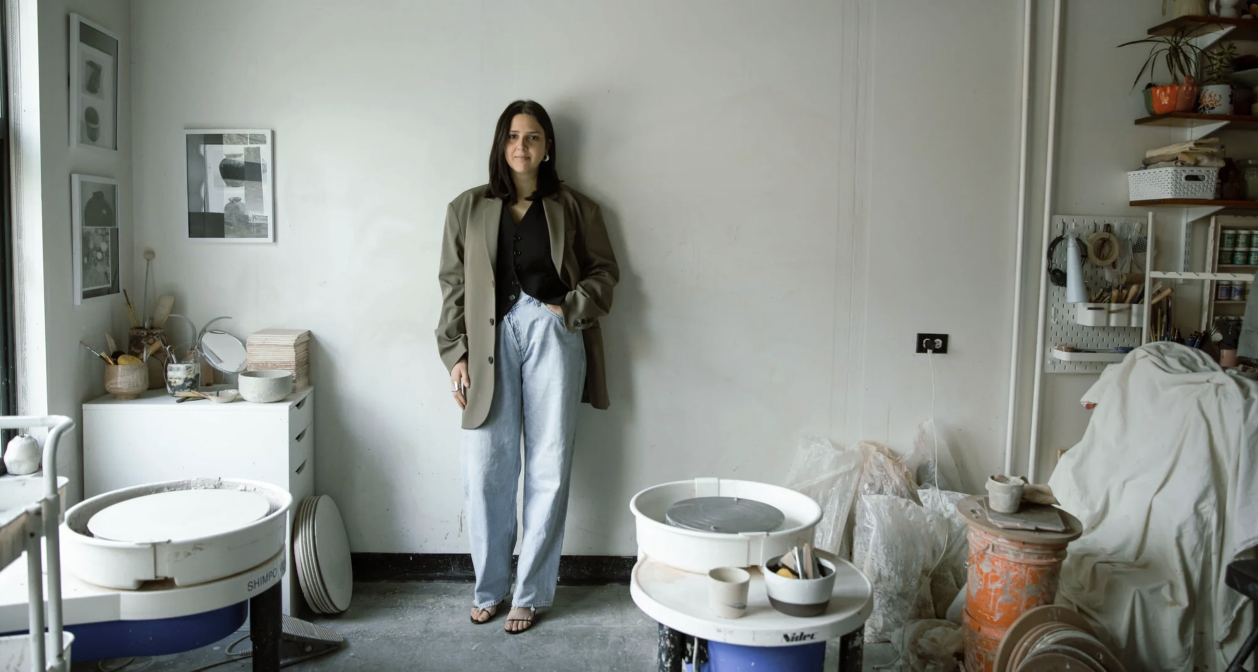 A woman standing inside an art studio or ceramics workspace, surrounded by pottery equipment and supplies.