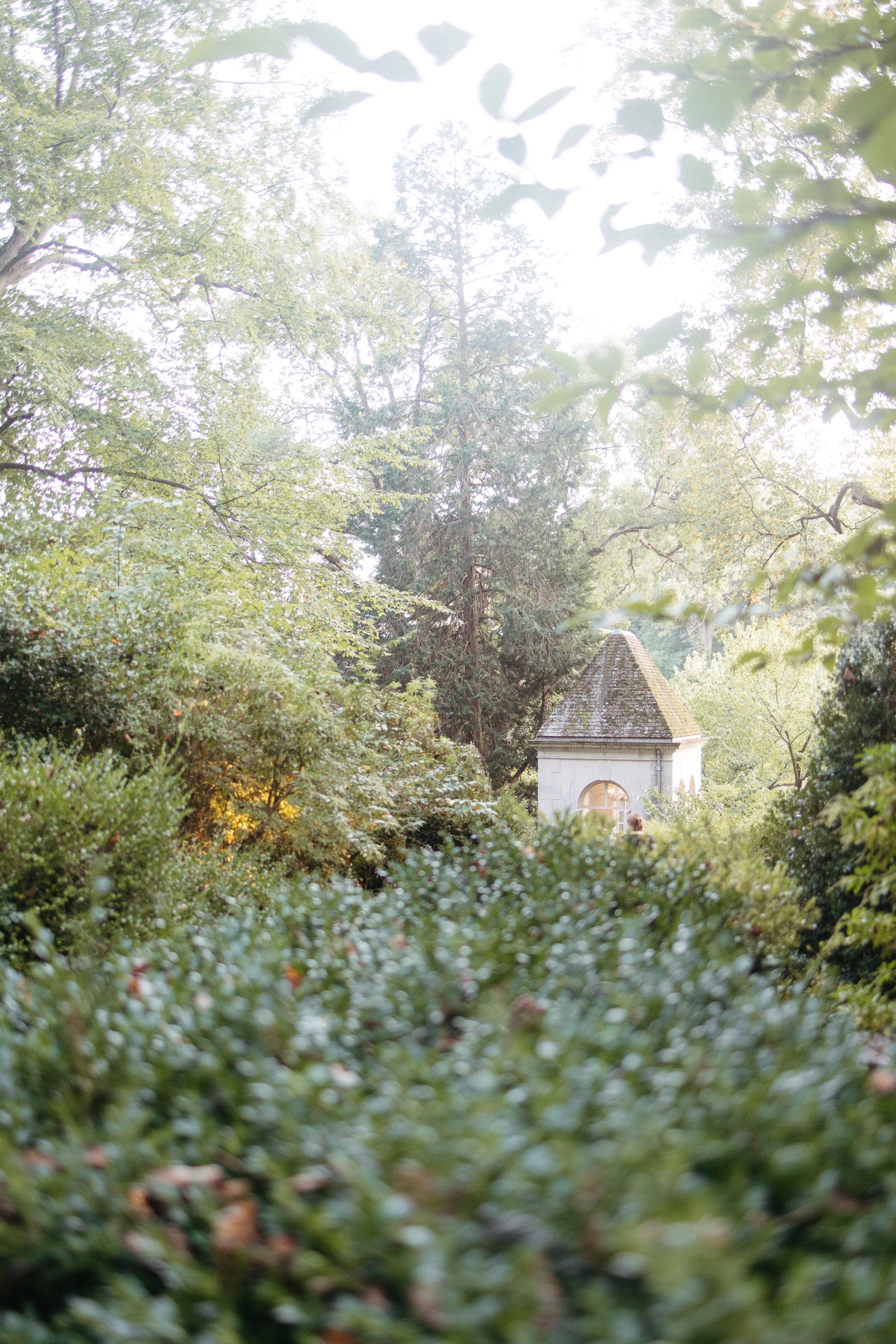 A serene view of the Winterthur gardens, showcasing a picturesque stone chapel nestled among vibrant greenery. Kathleen is a luxury wedding photographer offering documentary and editorial style wedding photography in New York, Delaware, Maryland, and
