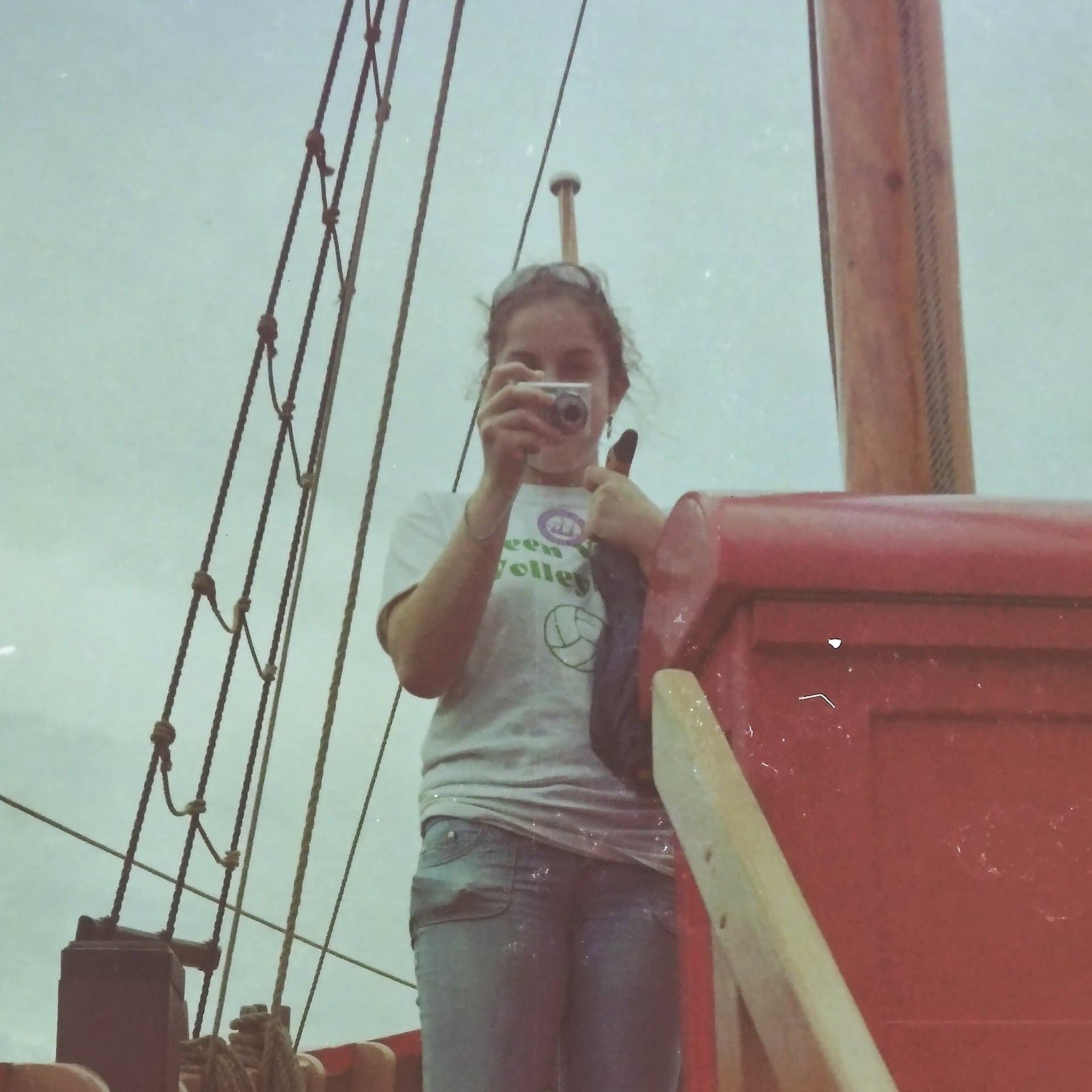 A young Kathleen taking a photo aboard a ship, with ship rigging and a wooden mast visible in the background.