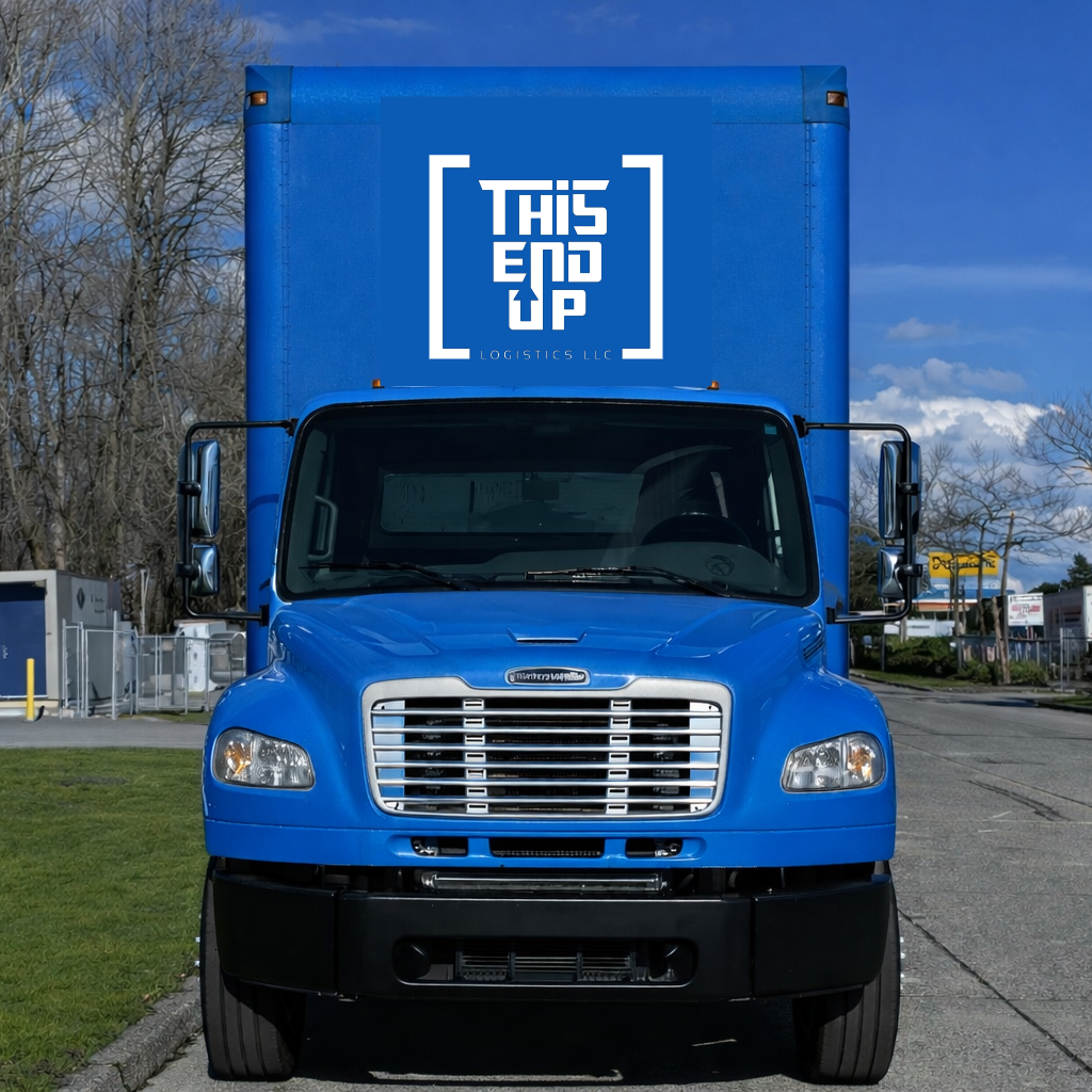 A blue delivery truck with a large box on the back displaying the words 'THIS END UP' and 'LOGISTICS LLC' in white text. The truck is parked on a street with trees and buildings in the background, under a partly cloudy sky.