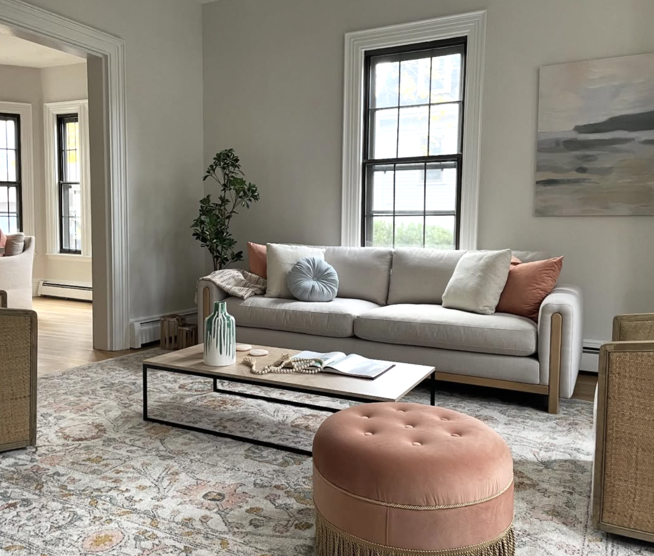 A living room with teal and peach accents, a fringed ottoman and patterned oriental rug