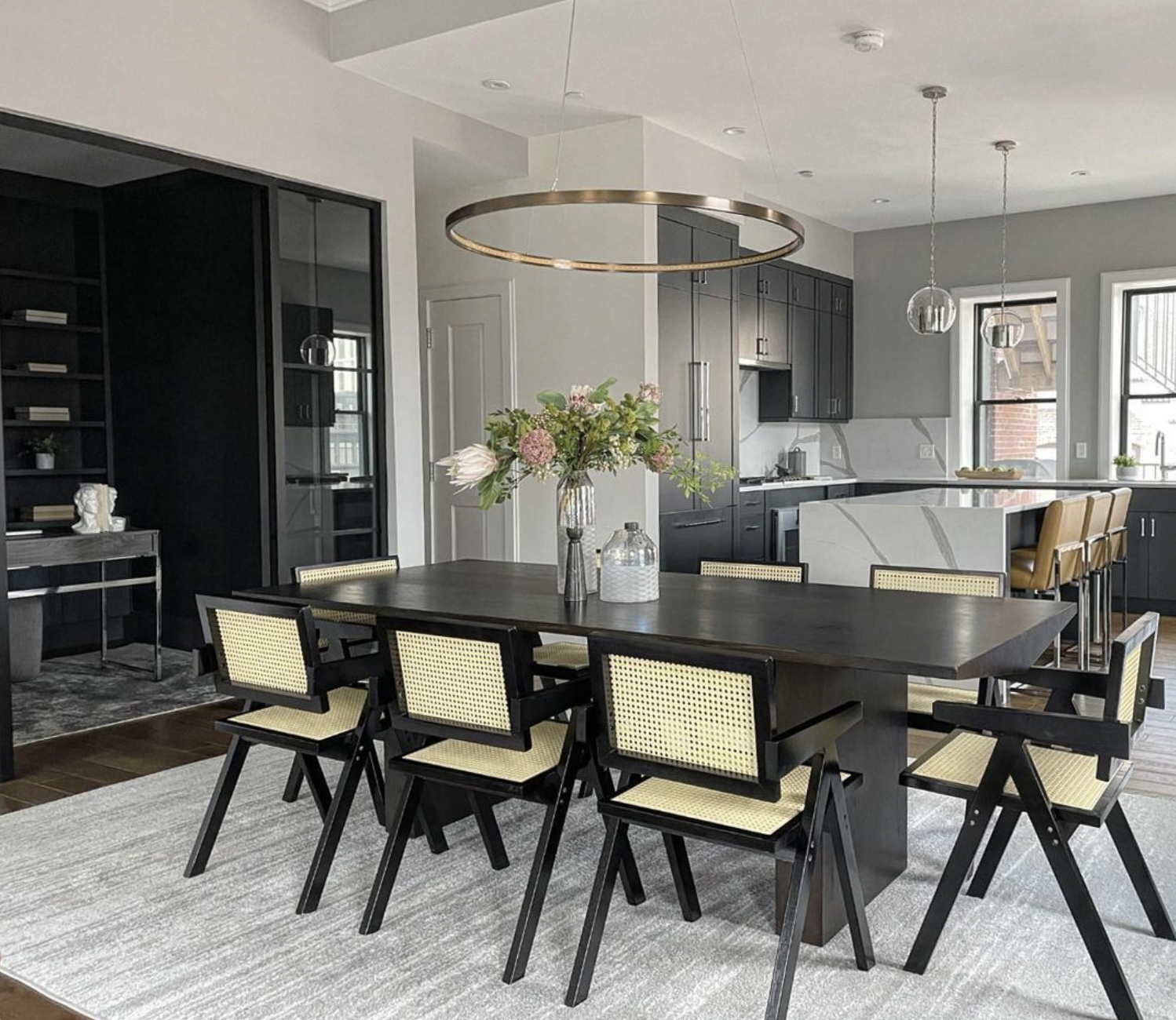 Black and rattan dining chairs at a beautiful black dining table in a high-end unit condo. Adjacent office is visible.