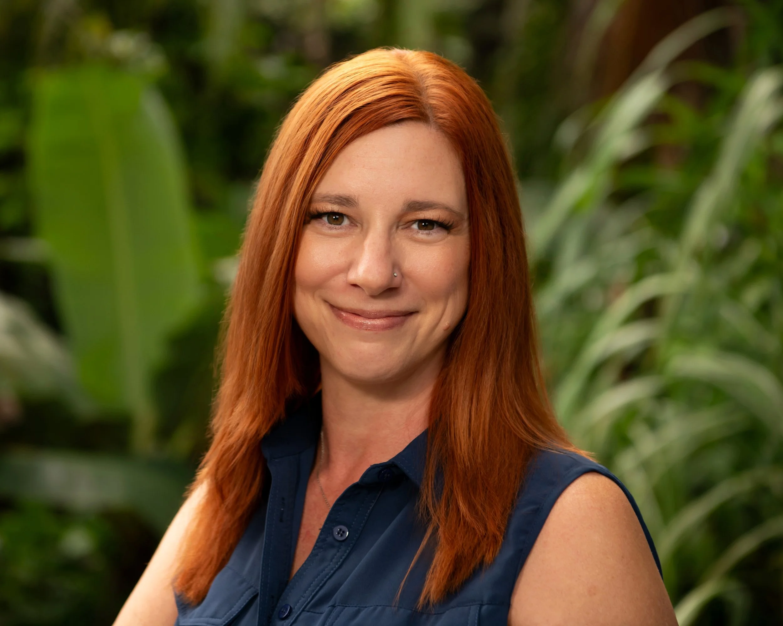 A woman with long reddish hair drinking from a dark gray mug while sitting outdoors in an urban setting.