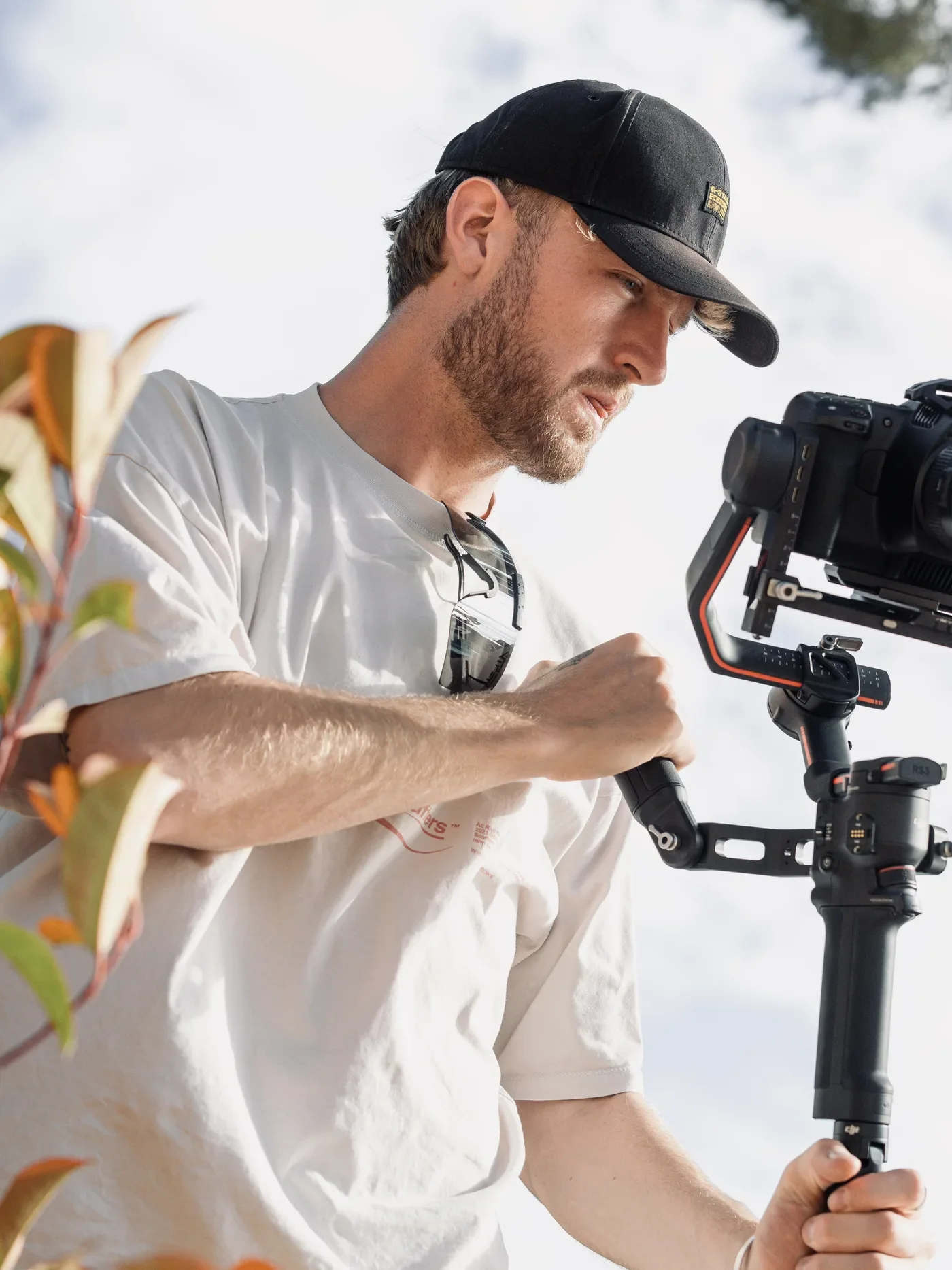 Jeune homme professionnel utilisant un stabilisateur pour caméra en extérieur, portant une casquette noire et des lunettes de soleil, en train de filmer.