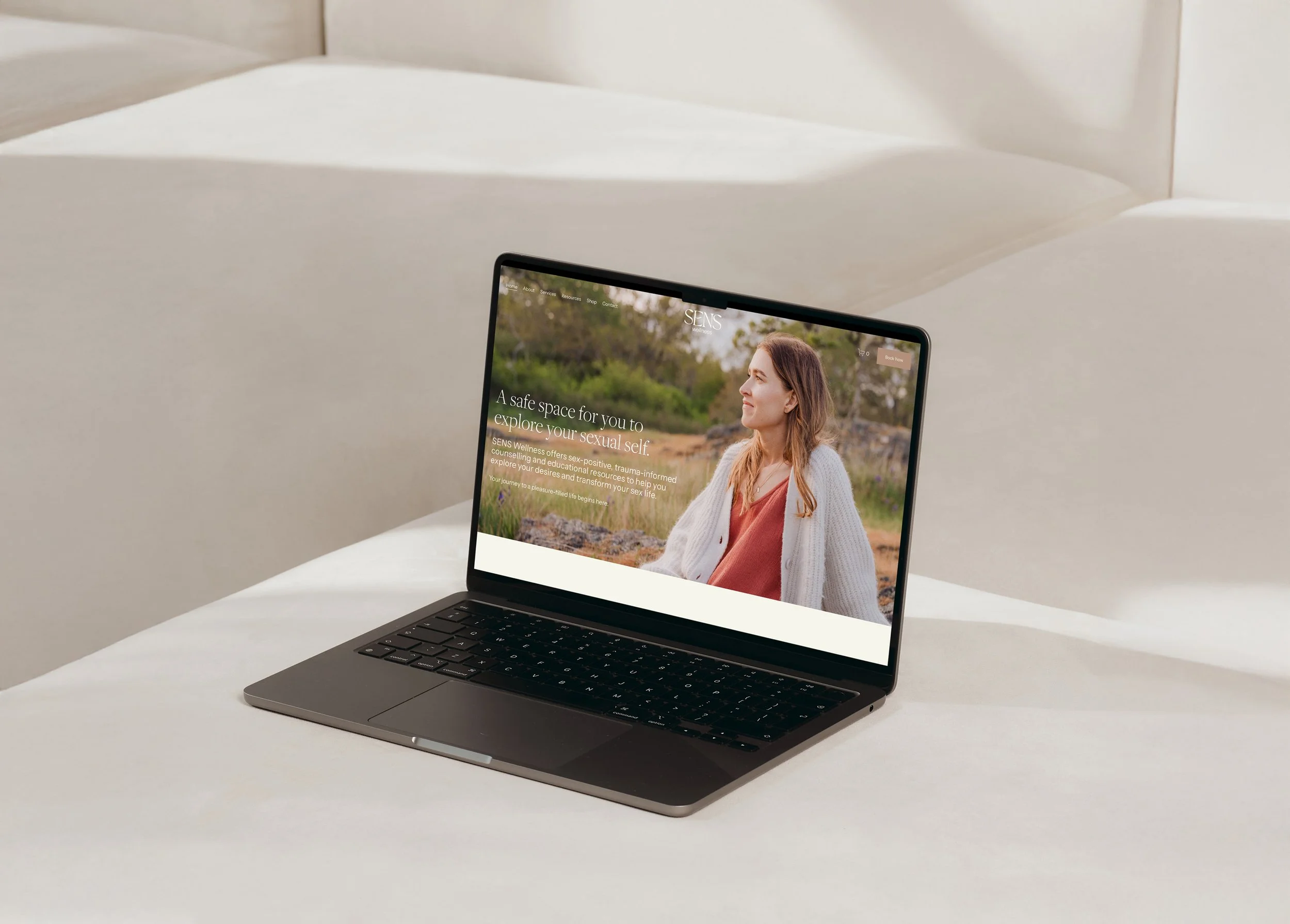 A laptop on a white bed displaying a website for SENS Wellness, featuring a woman outdoors with trees and greenery in the background.