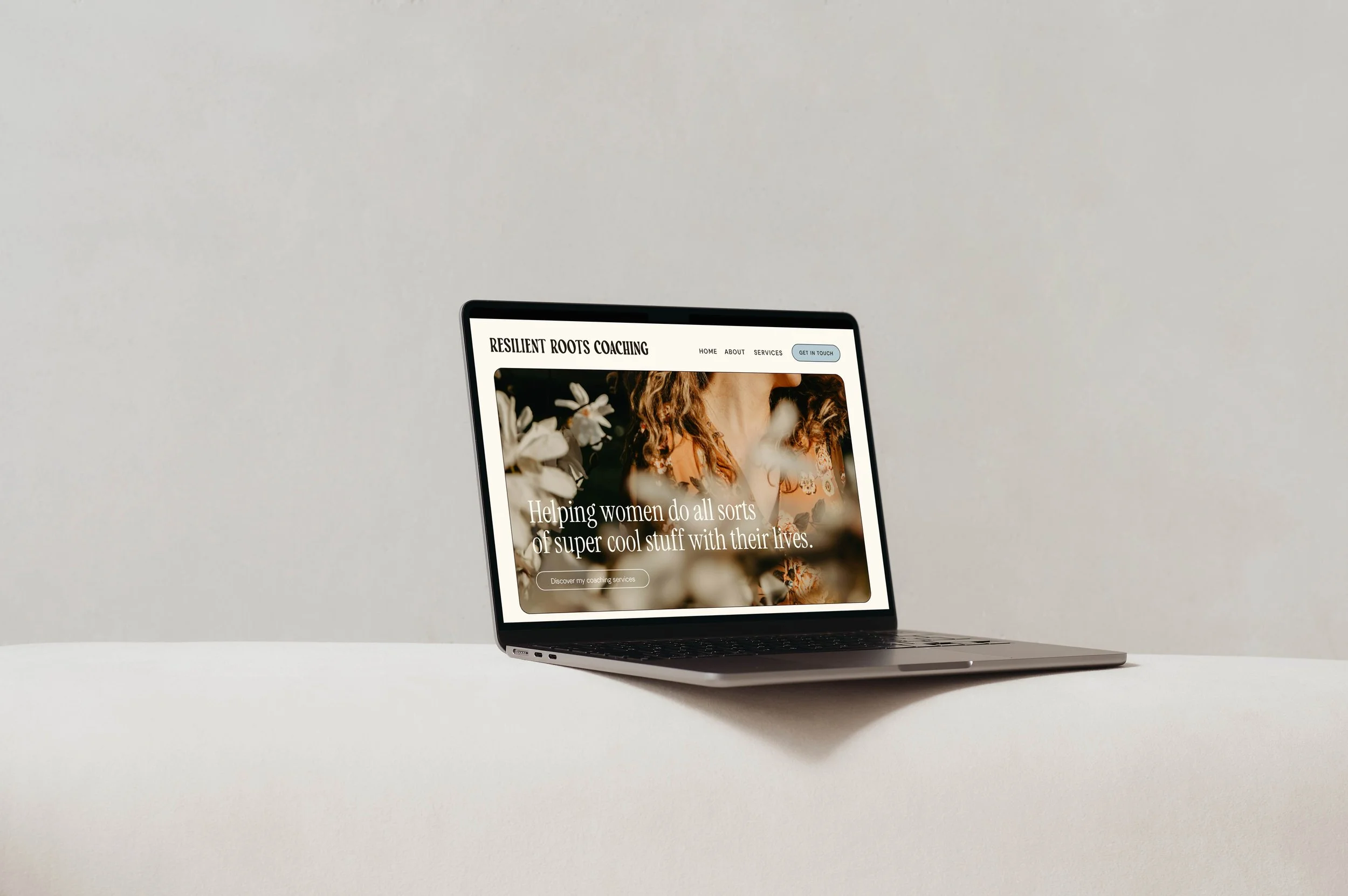 Open laptop displaying a website called 'Resilient Roots Coaching' with a background image of a woman with curly hair surrounded by flowers.