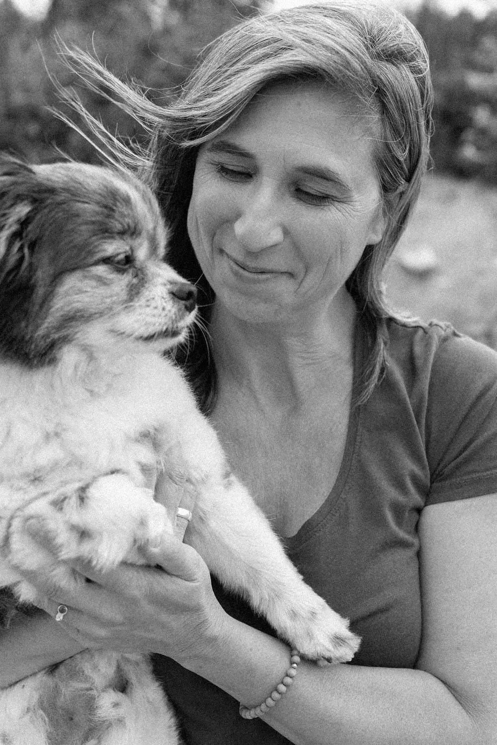 A woman holding an Australian Shepherd puppy close to her face outdoors, smiling with her eyes closed.
