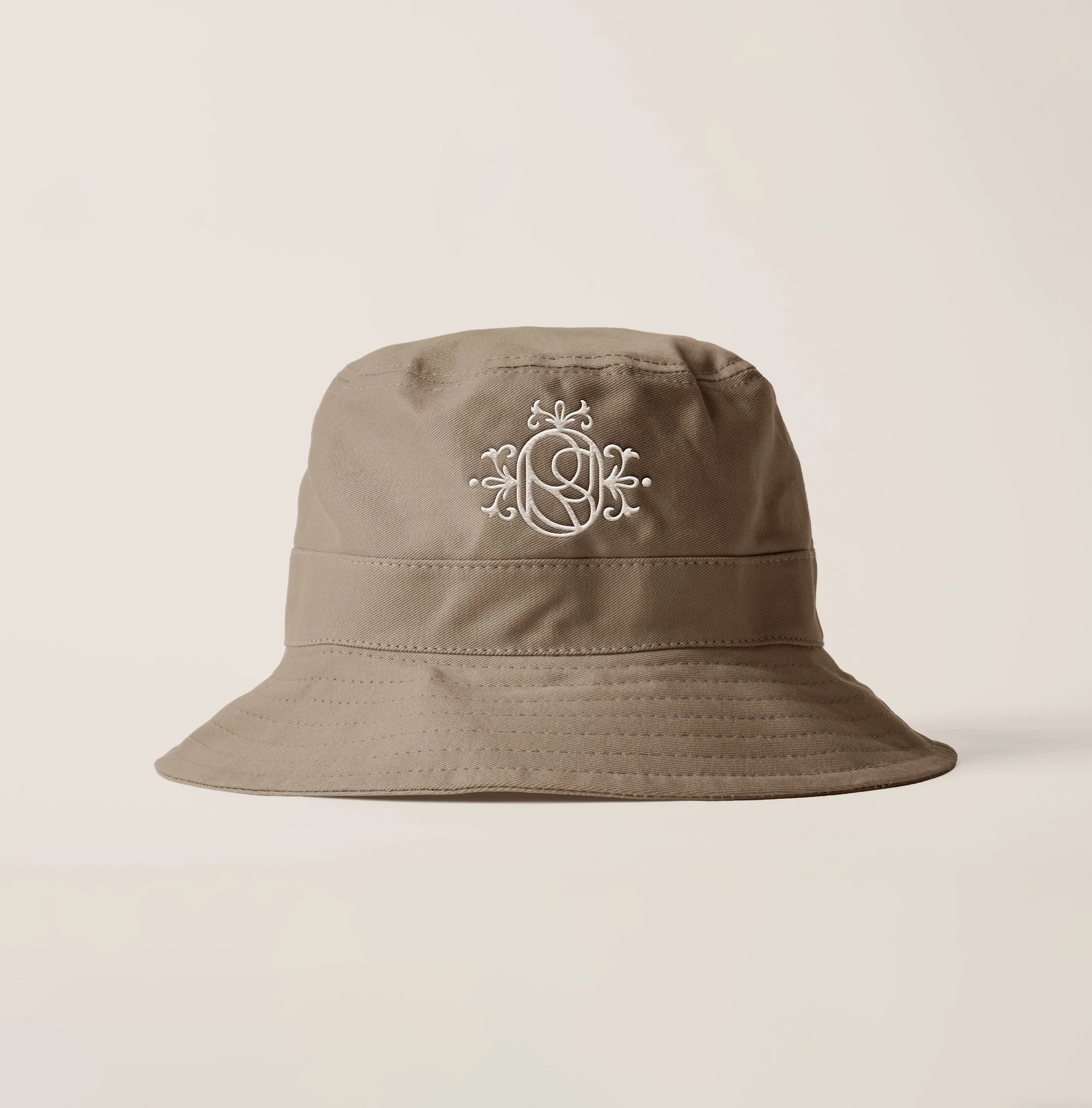 Beige bucket hat with white embroidered monogram design on the front.