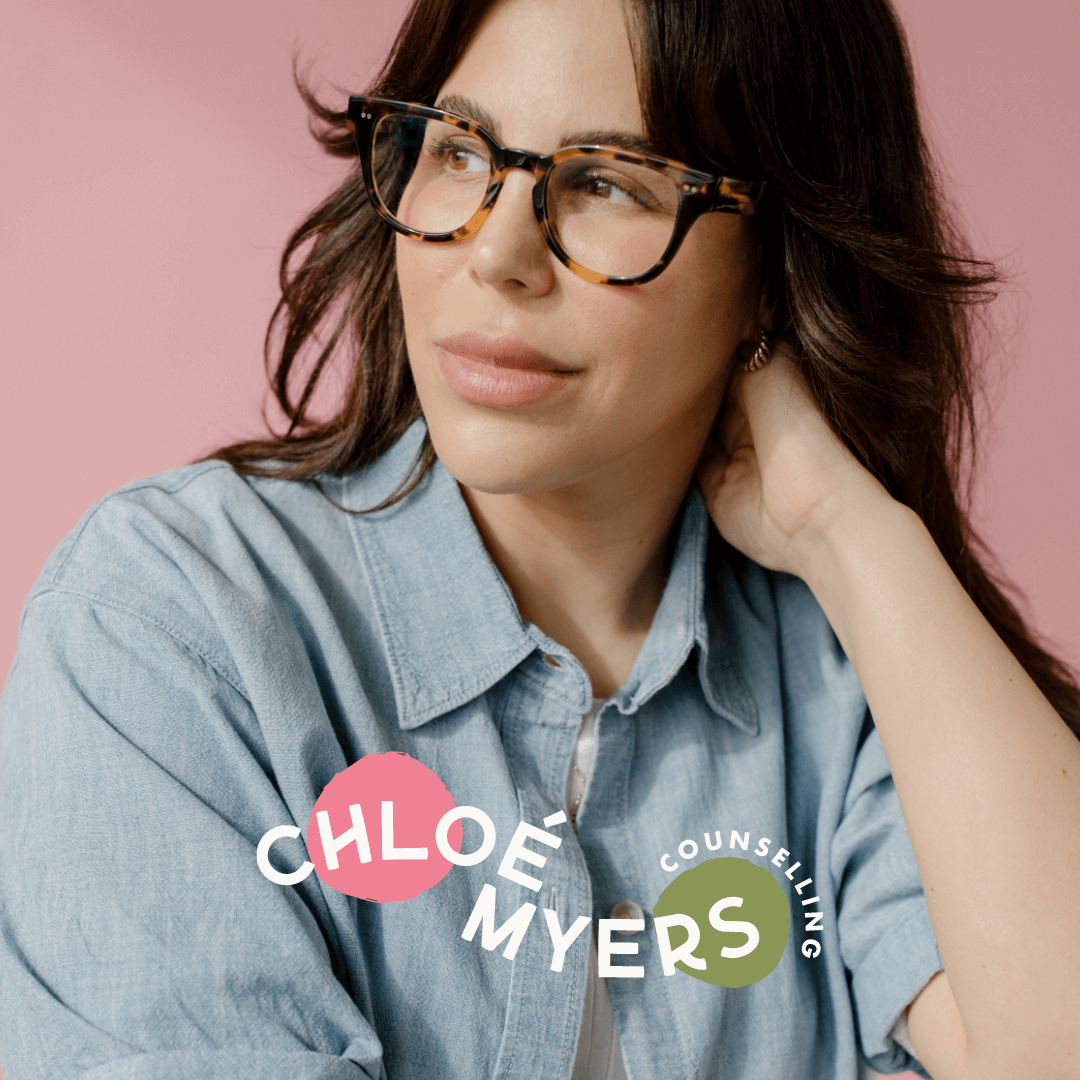 A woman with wavy brunette hair wearing tortoise-shell glasses and a light blue denim shirt, looking to the side against a pink background, with the text "Chloe Myers Counseling" overlaid.