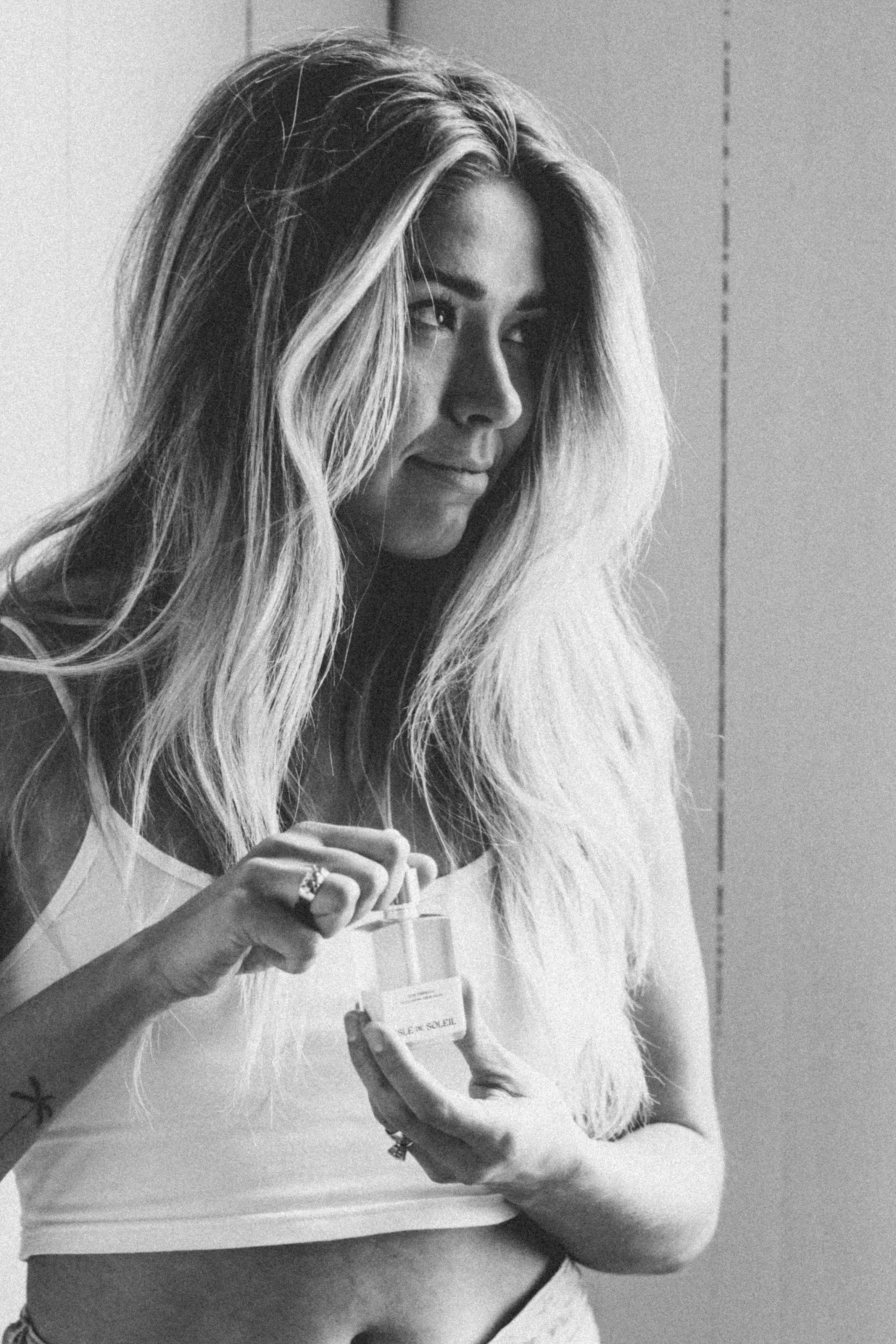 Black and white photo of a woman with long hair holding a bottle of perfume in a dropper bottle.