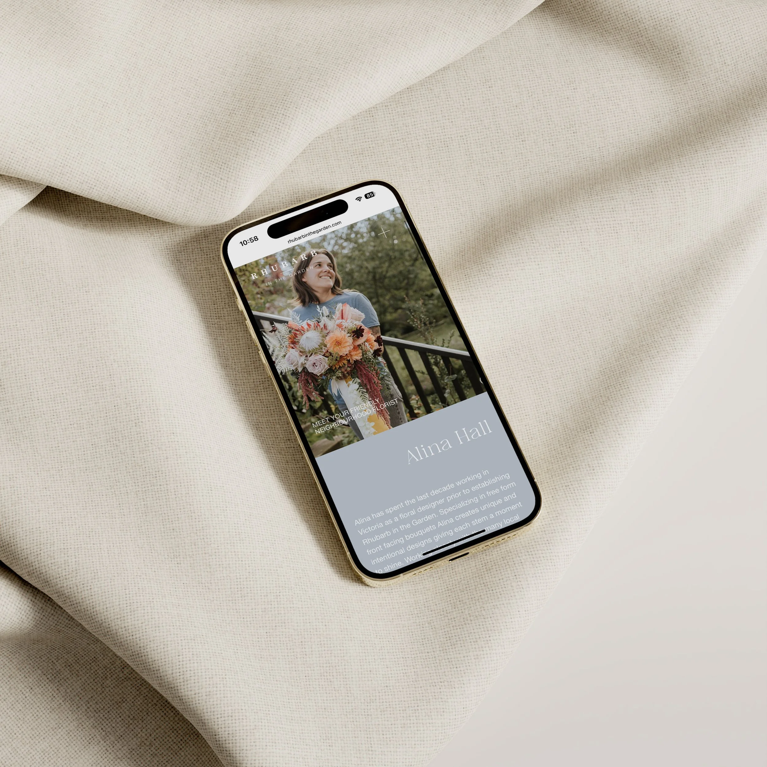 Smartphone displaying a webpage with a woman holding a floral bouquet, standing outdoors with trees in the background, on a light-colored fabric surface.