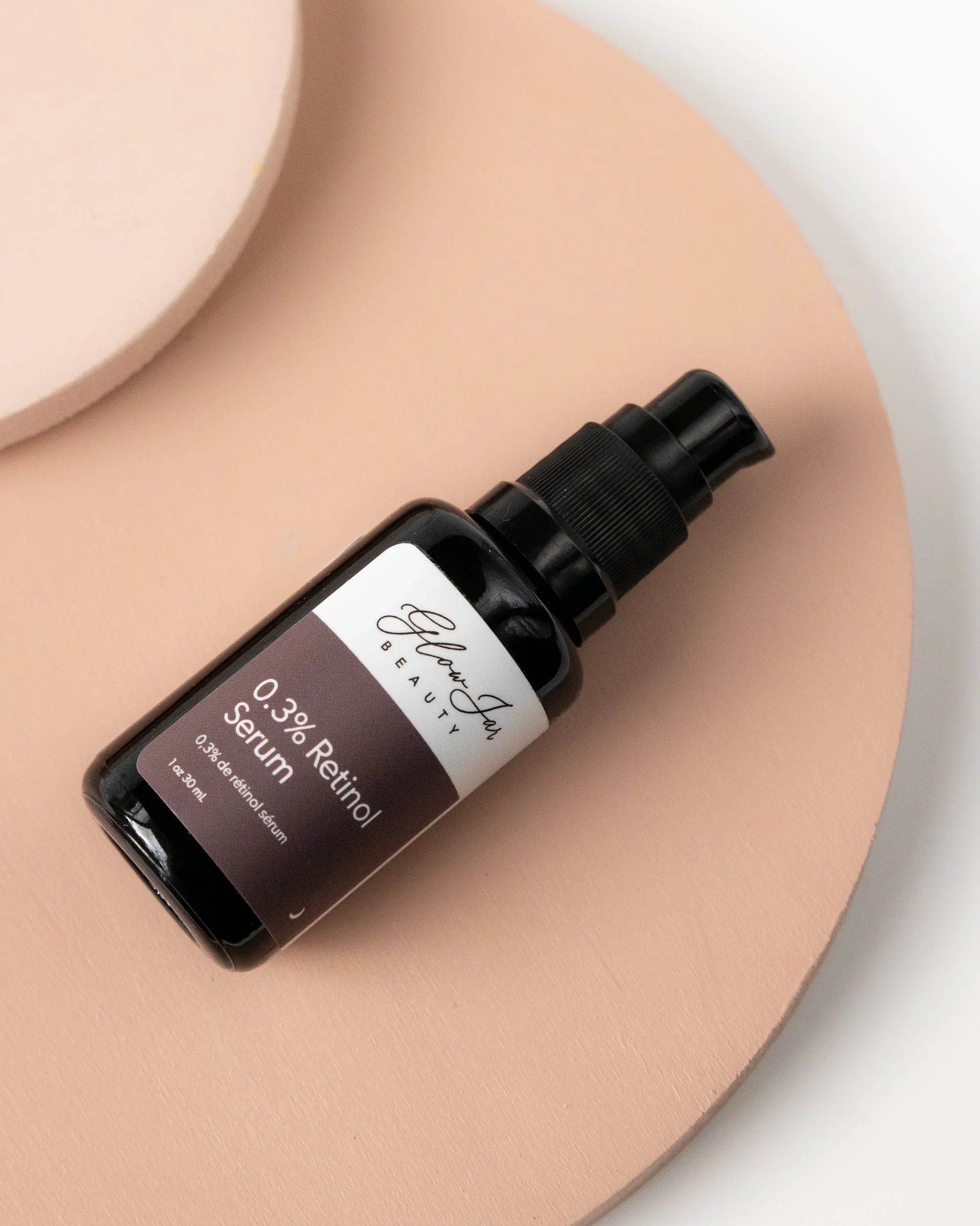 Black bottle of Glow Girl Beauty 0.3% Retinol Serum on pink and white background.