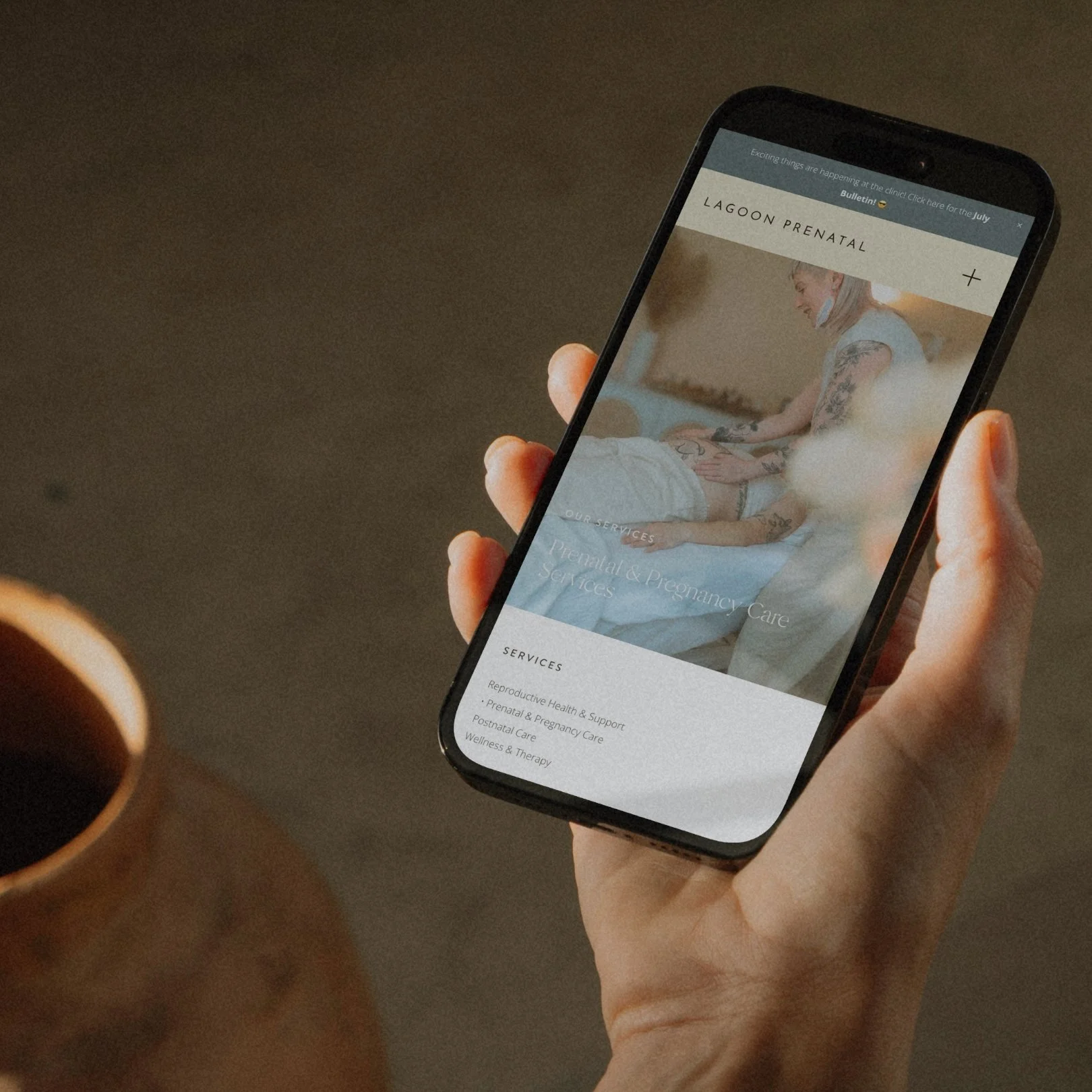 A person holding a smartphone displaying a prenatal and pregnancy care service website for Lagoon Prenatal. The website shows a woman receiving prenatal care.