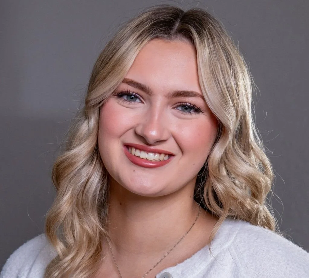 A woman with long, wavy brown hair smiling at the camera, showing her teeth.