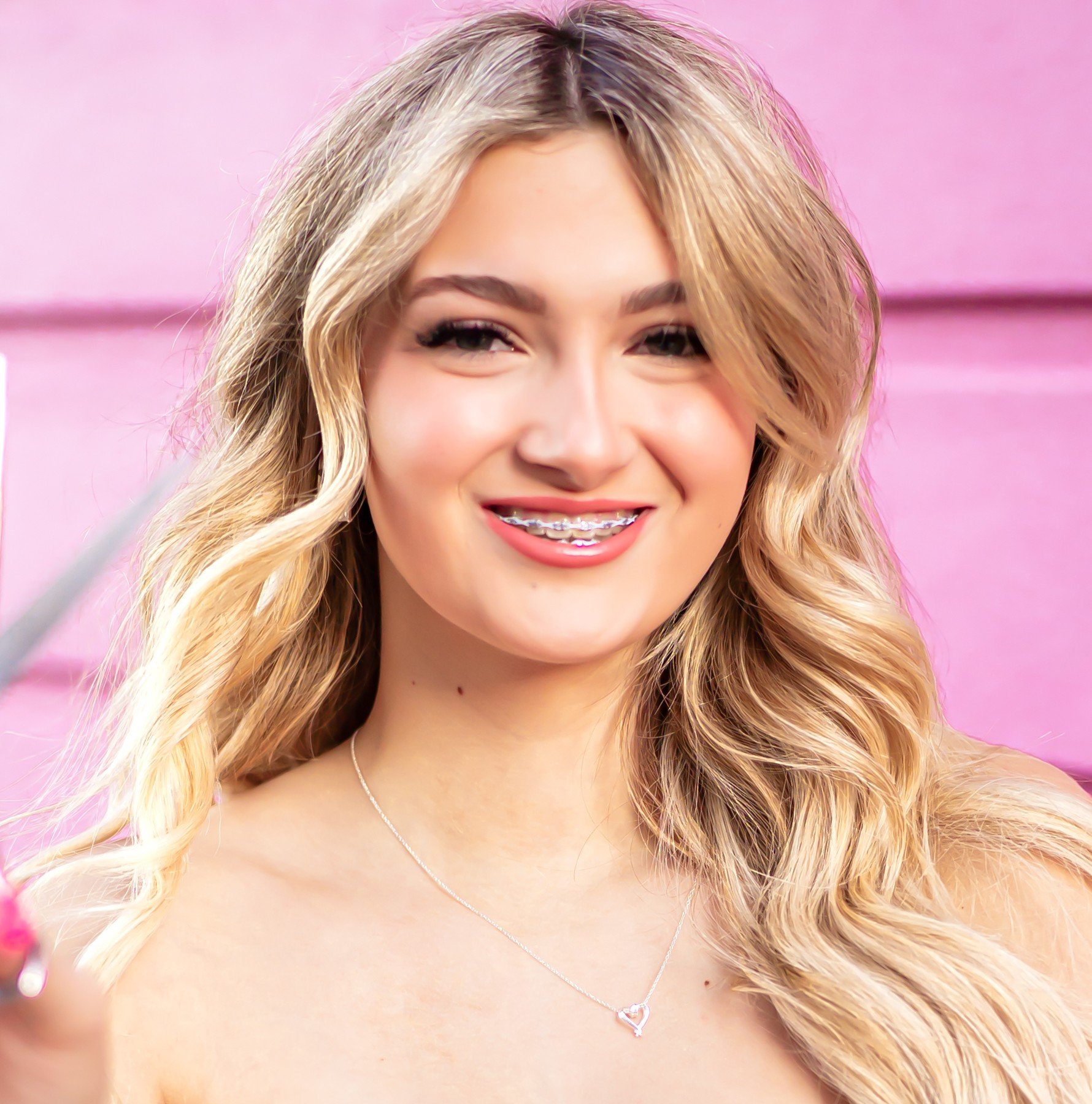 A woman with long, wavy brown hair smiling at the camera, showing her teeth.