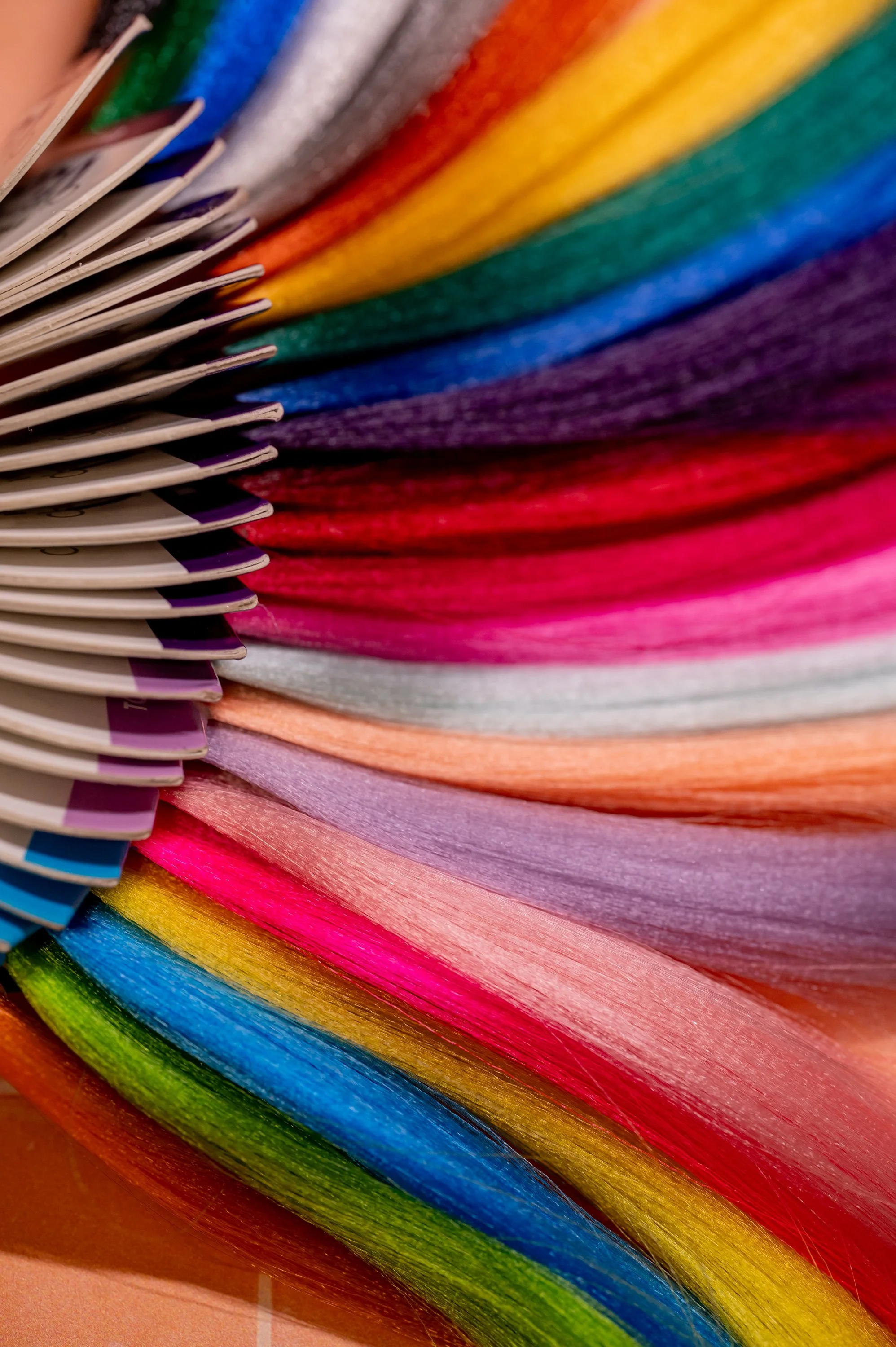 A close-up of a color wheel on a color fan deck with various shades of Hair Extensions in bright, vibrant colors including pink, red, orange, yellow, green, blue, purple, and gray. Moxxi Grey offers Hair extensions, Hair Salon Services in DFW