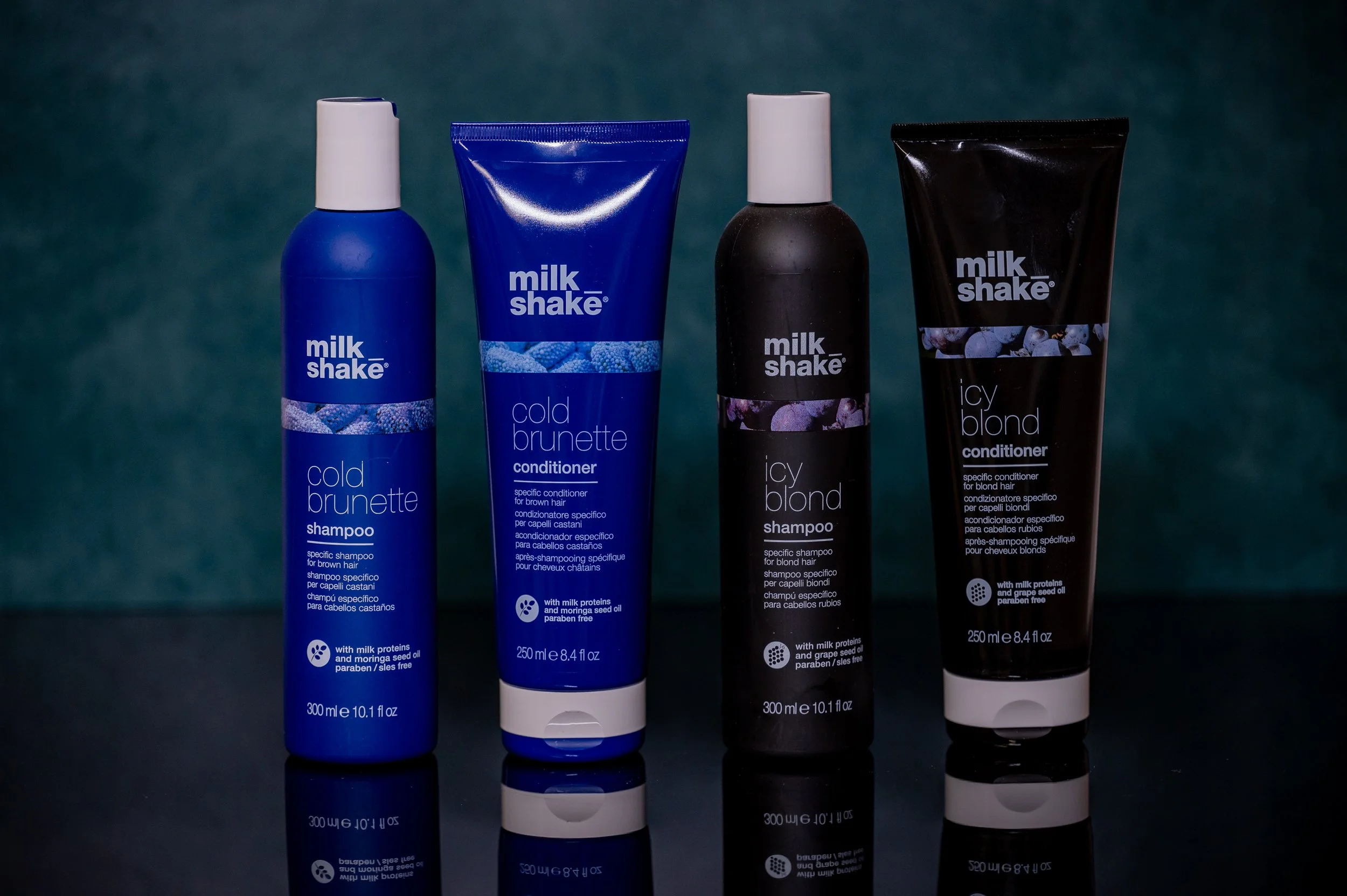 Four bottles and tubes of Milk Shake brand hair care products, including two blue bottles and two black tubes, labeled 'cold brunette' and 'icy blond', Sold at Moxxi Grey Salon in Colleyville, TX