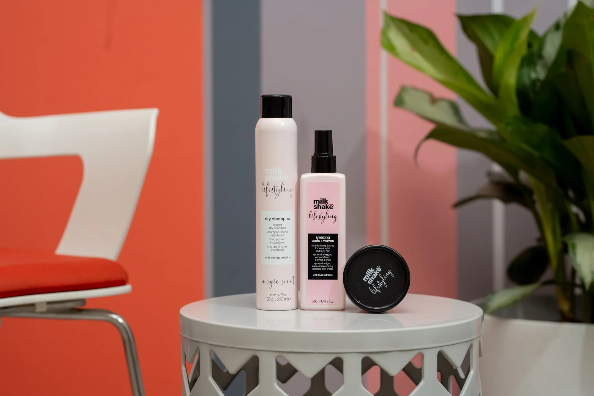 Three Milk Shake hair styling products on a white table: a dry shampoo, a curl spray, sold and used at Moxxi Grey Salon in Colleyville, TX Leading Hair stylists and expert Hairdressers offering top-rated Hair styling services in DFW