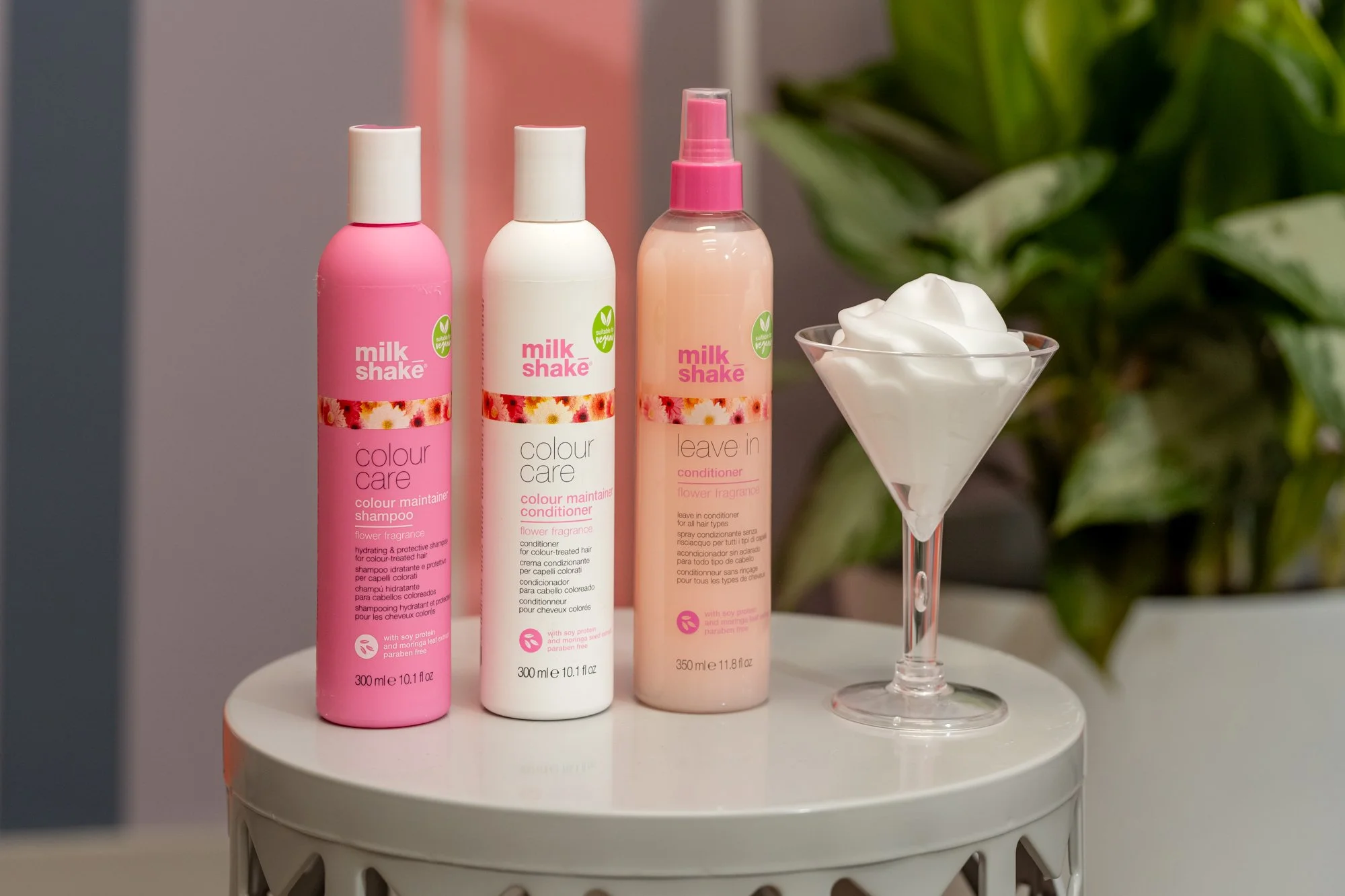 Three bottles of Milk Shake hair products, a pink shampoo, a white conditioner, and a pink leave-in conditioner, sold at Moxxi Grey Salon in Colleyville, TX