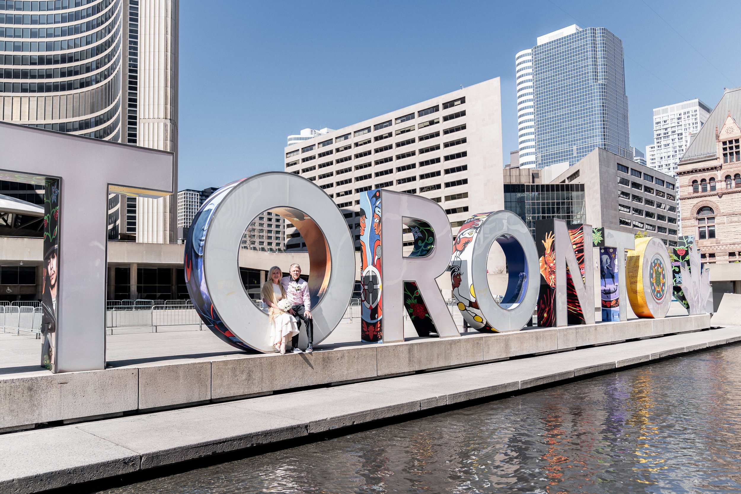 Bride and groom smiling in front of Nathan Phillips Square