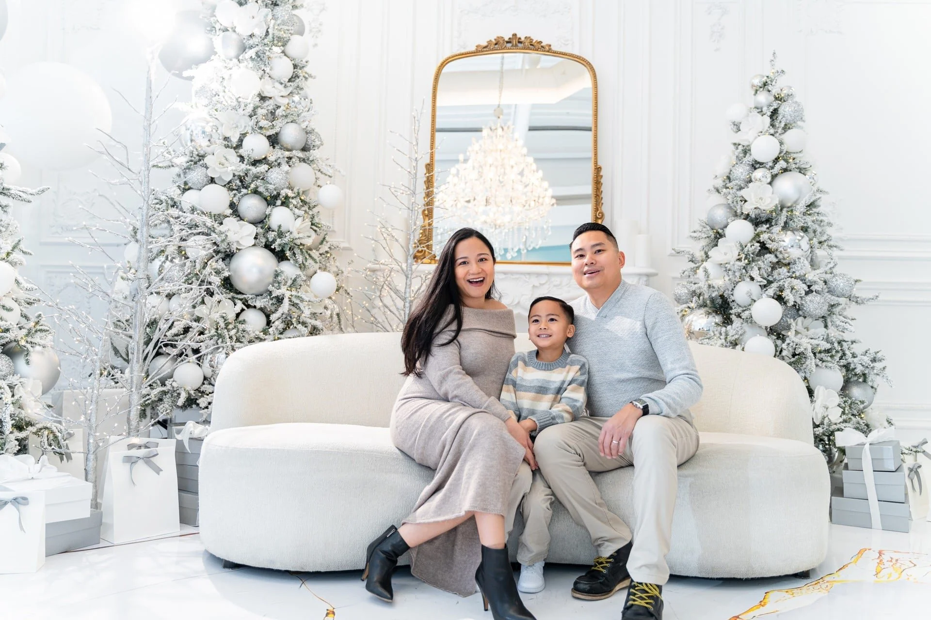 Family Christmas photoshoot on a white curved sofa among flocked trees, Toronto