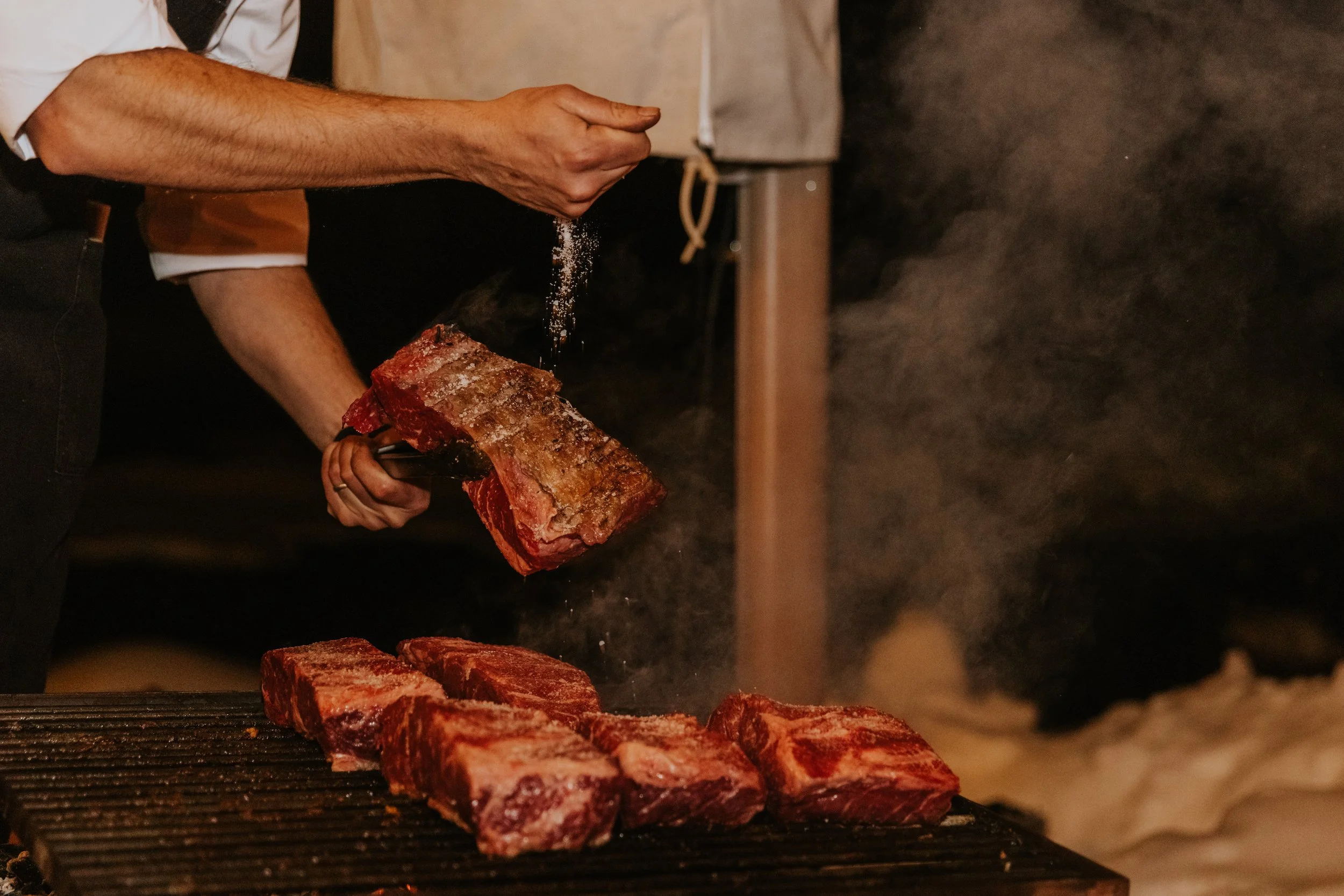 Chef seasoning beef on grill at night