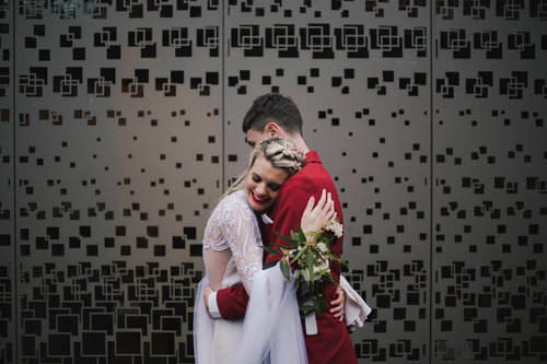groom in red suit embracing his blonde haired bride