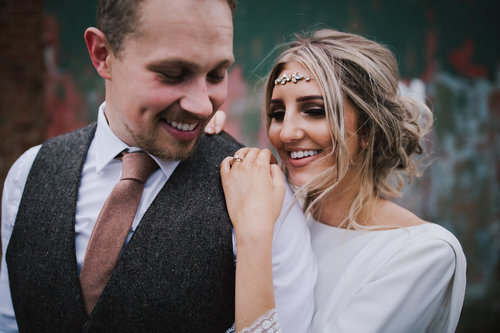 a smiling portrait of a bride wearing a head chain and her groom 