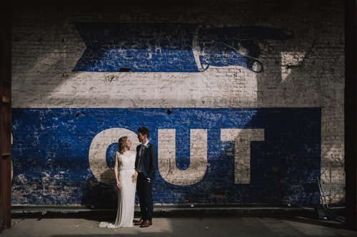 a sunlit blue and white wall mural with a bride and groom standing in front of it