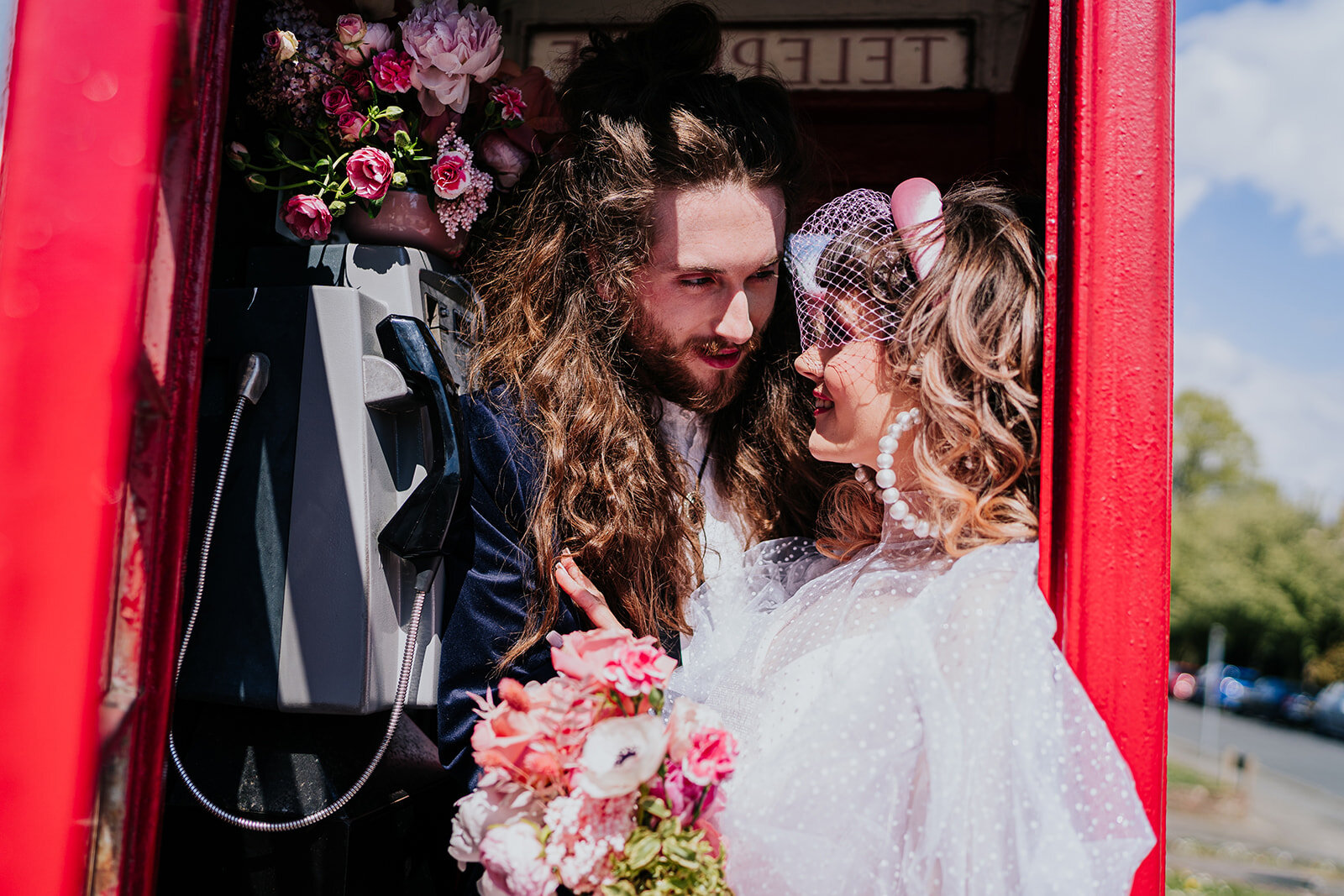 a bride and groom in a flower filled red telephone box