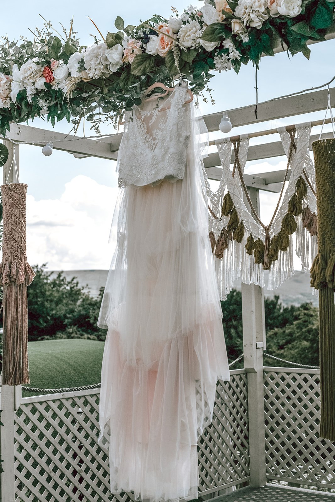 a frilly wedding dress hanging up on a wooden structure with floral decoration