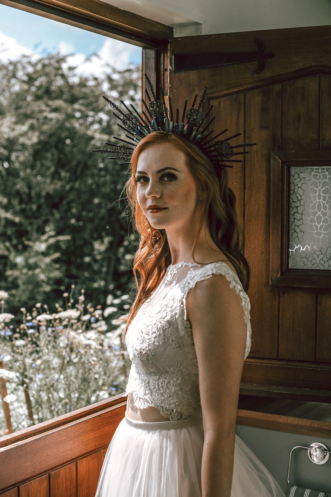 a red haired bride stood next to a door wearing an alternative crown