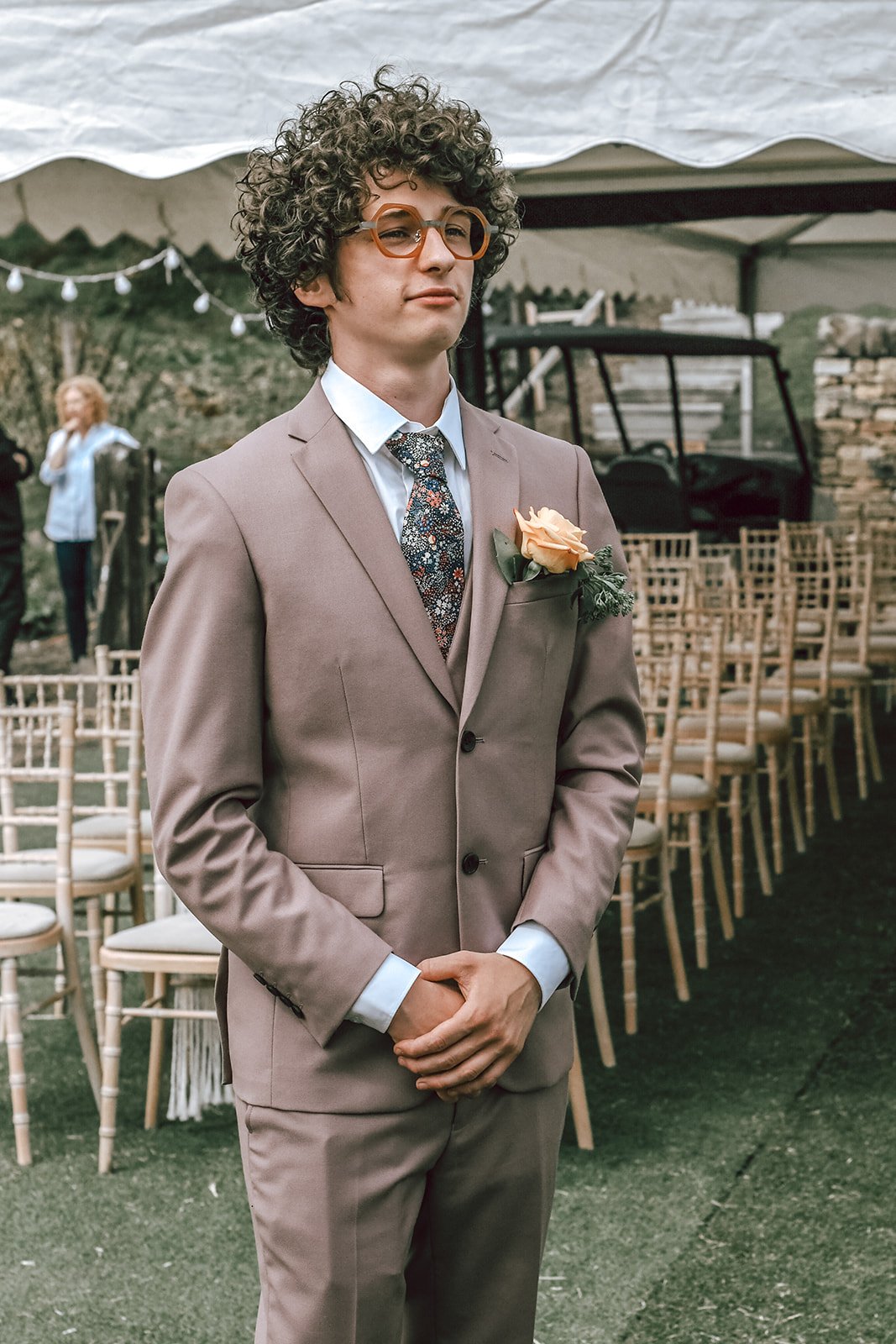 a curly haired groom wearing glasses and and a tweed suit