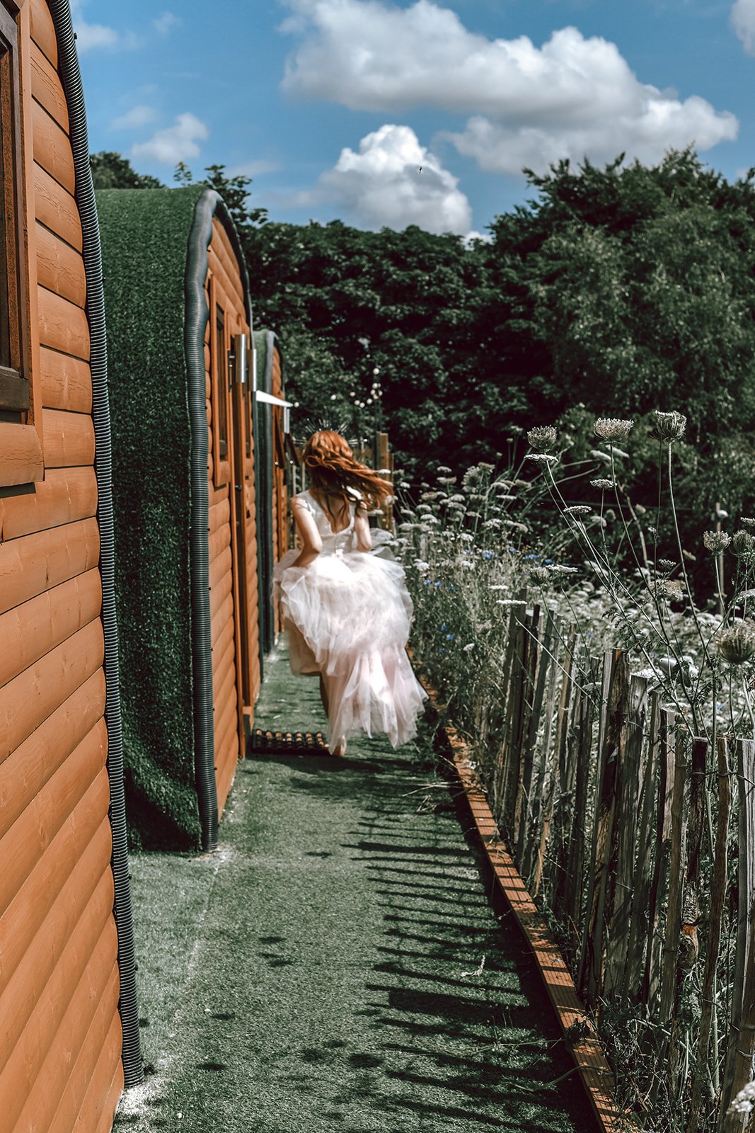 a red haired bride running through the countryside next to some wooden huts