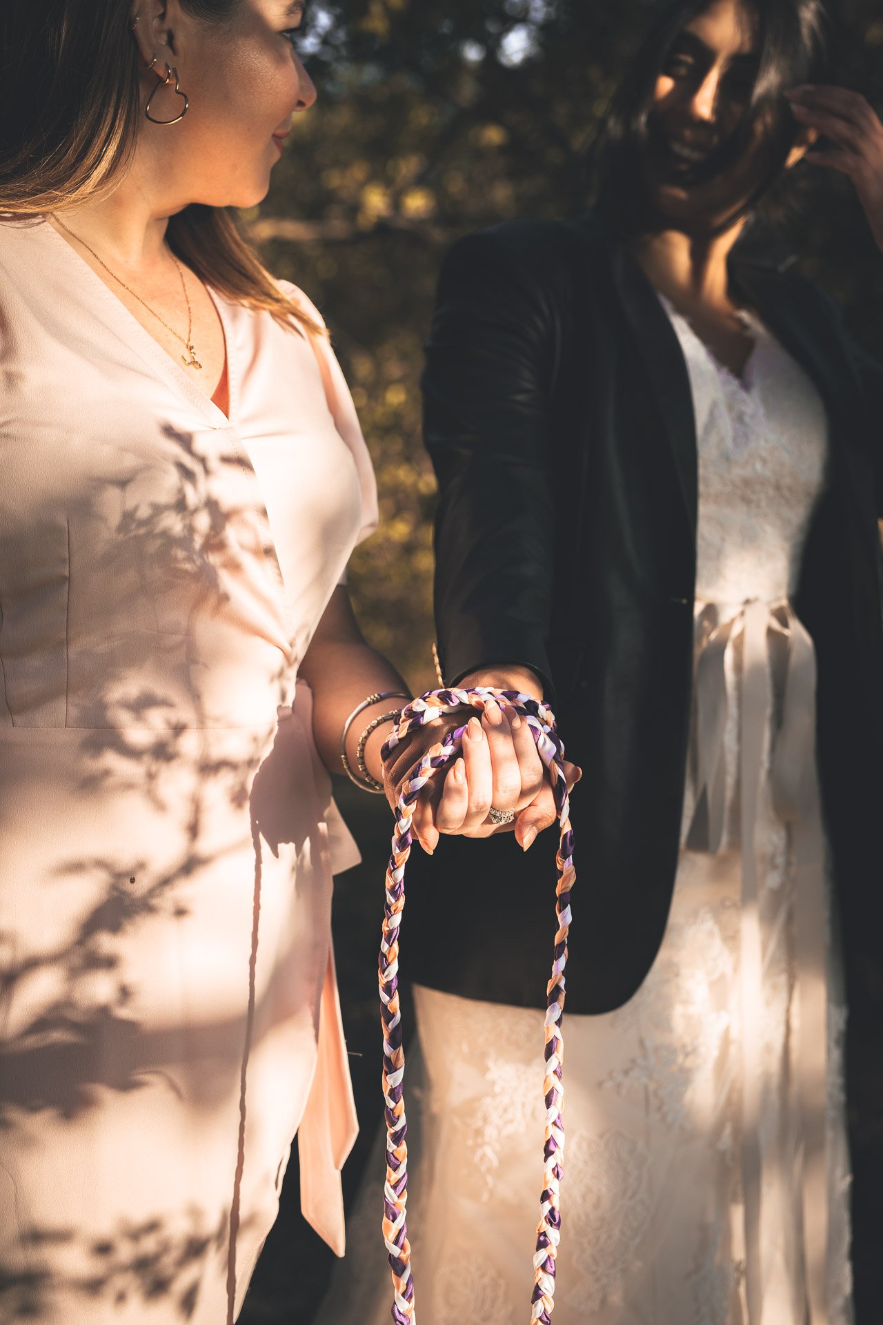  2 brides with their hands held and bound with a colorful ribbon for a handfasting ceremony. 