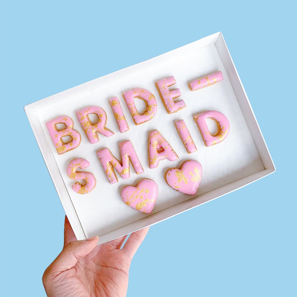  A white gift box of pink customised cookies that spell the word BRIDESMAID 